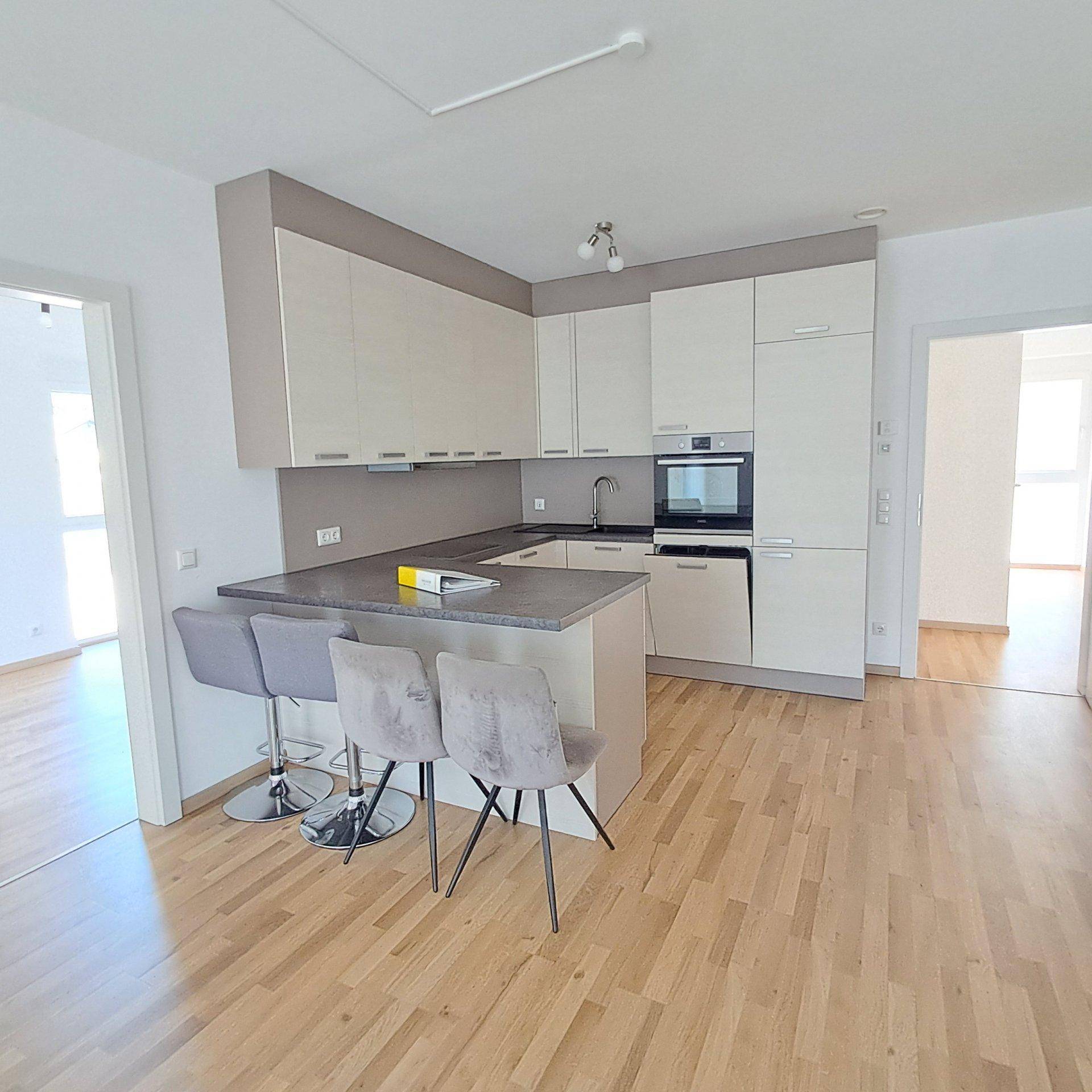 Moderne Einbauküche mit Kücheninsel, Frühstücksbar und hellem Holzfußboden.