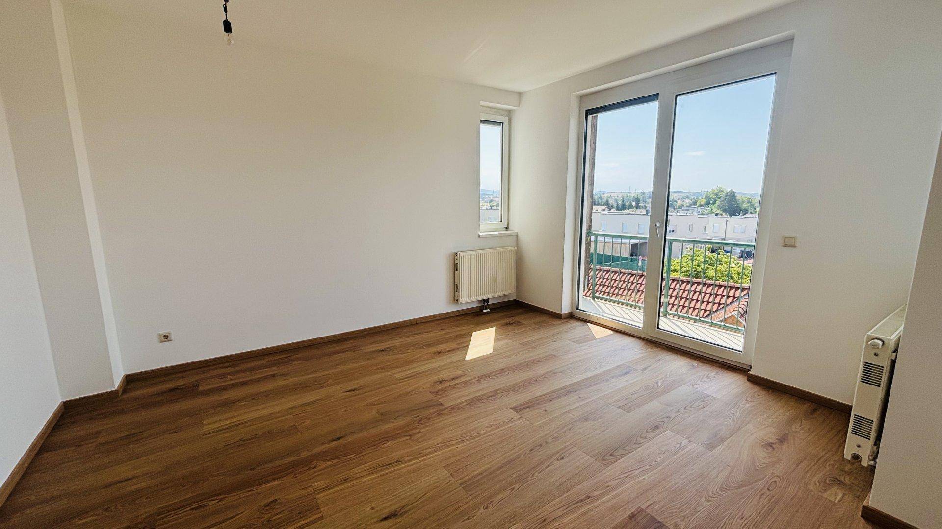 Lichtdurchfluteter Raum mit Holzfußboden und breiter Balkontür, die einen weiten Blick ermöglicht.
