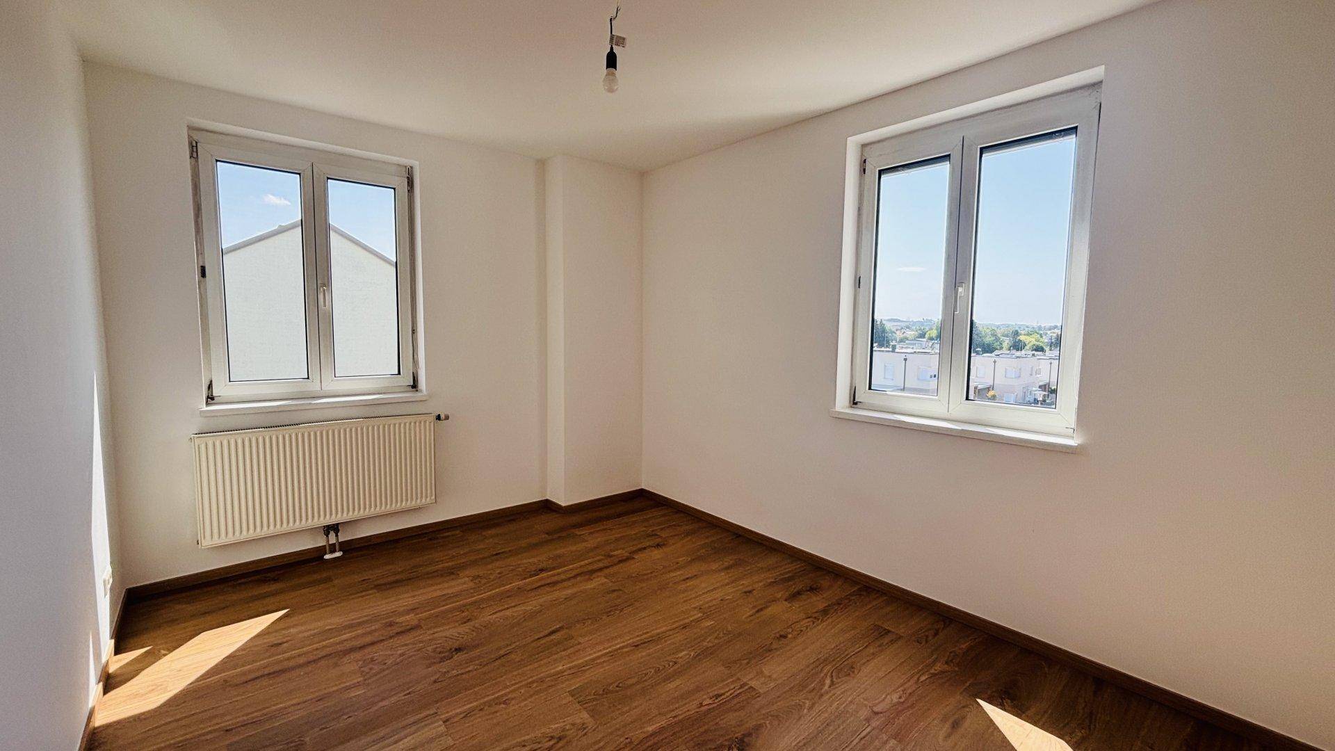 Helles Zimmer mit Holzfußboden und zwei Fenstern, die einen weiten Blick auf die Umgebung bieten.