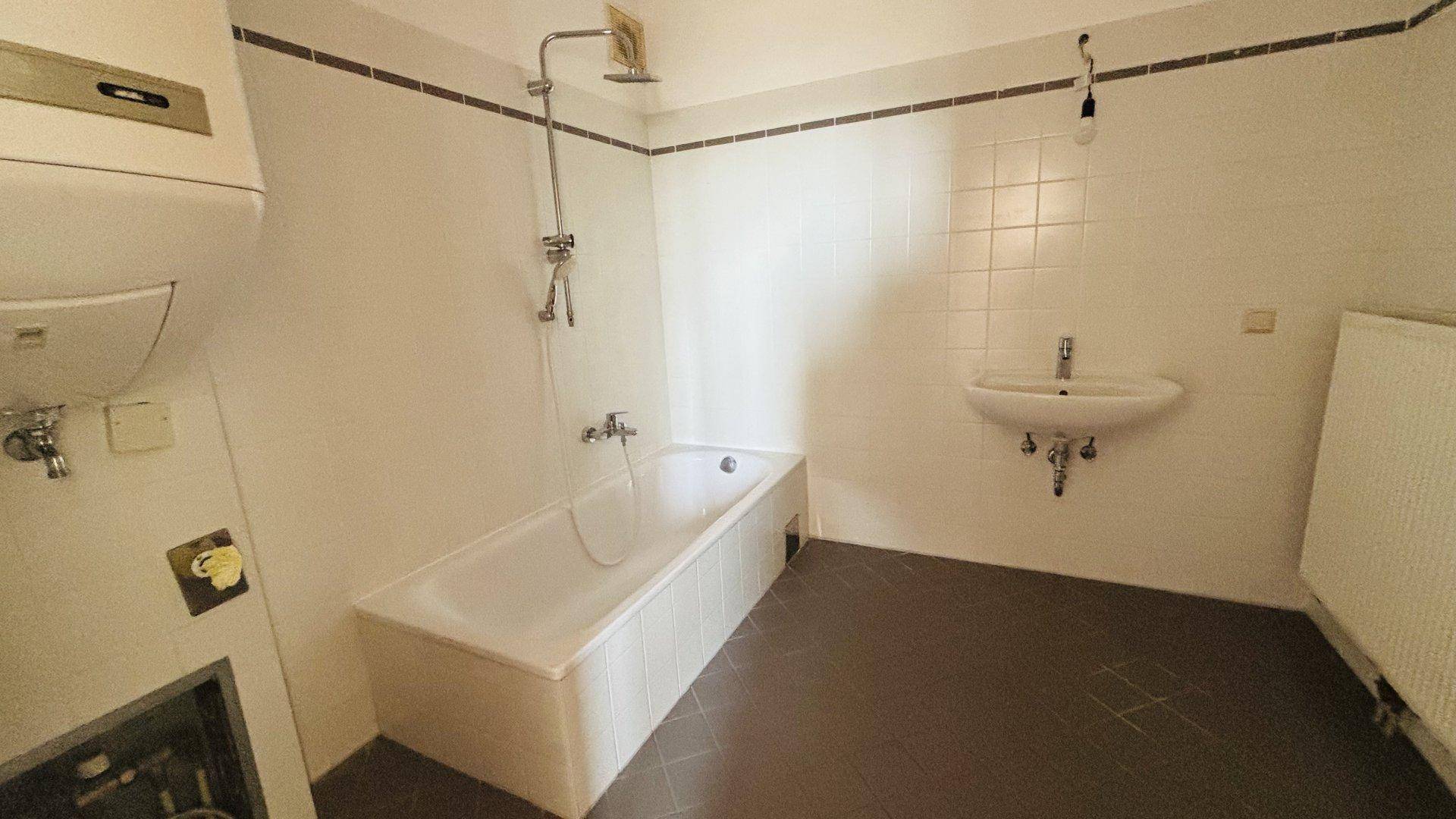 Badezimmer mit Badewanne, Waschbecken und weißen Fliesen, bereit zur Modernisierung.