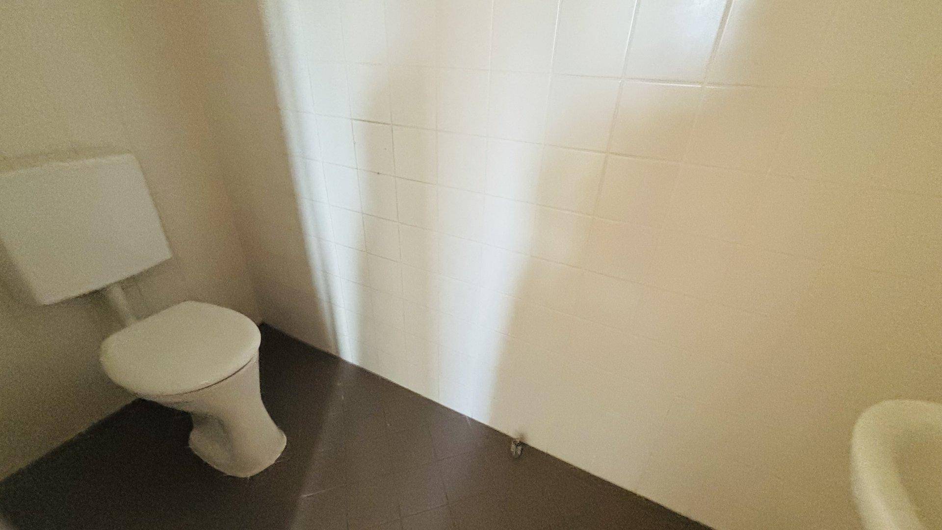 Einfaches WC mit Toilette und weißen Fliesen, funktional und sauber.