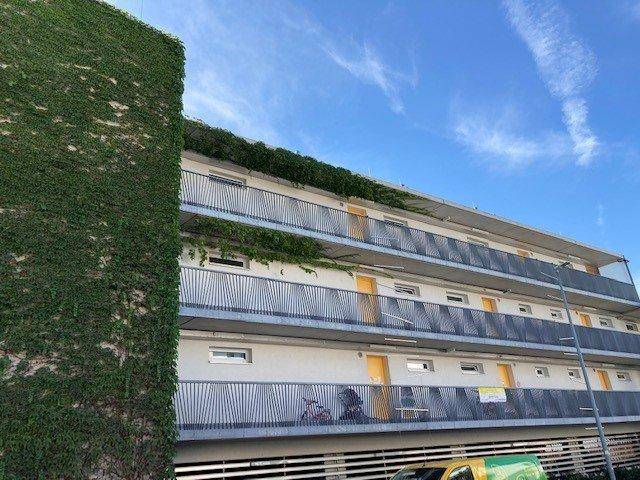Mehrstöckiges Wohngebäude mit zahlreichen Balkonen und einer teilweise begrünten Fassade.