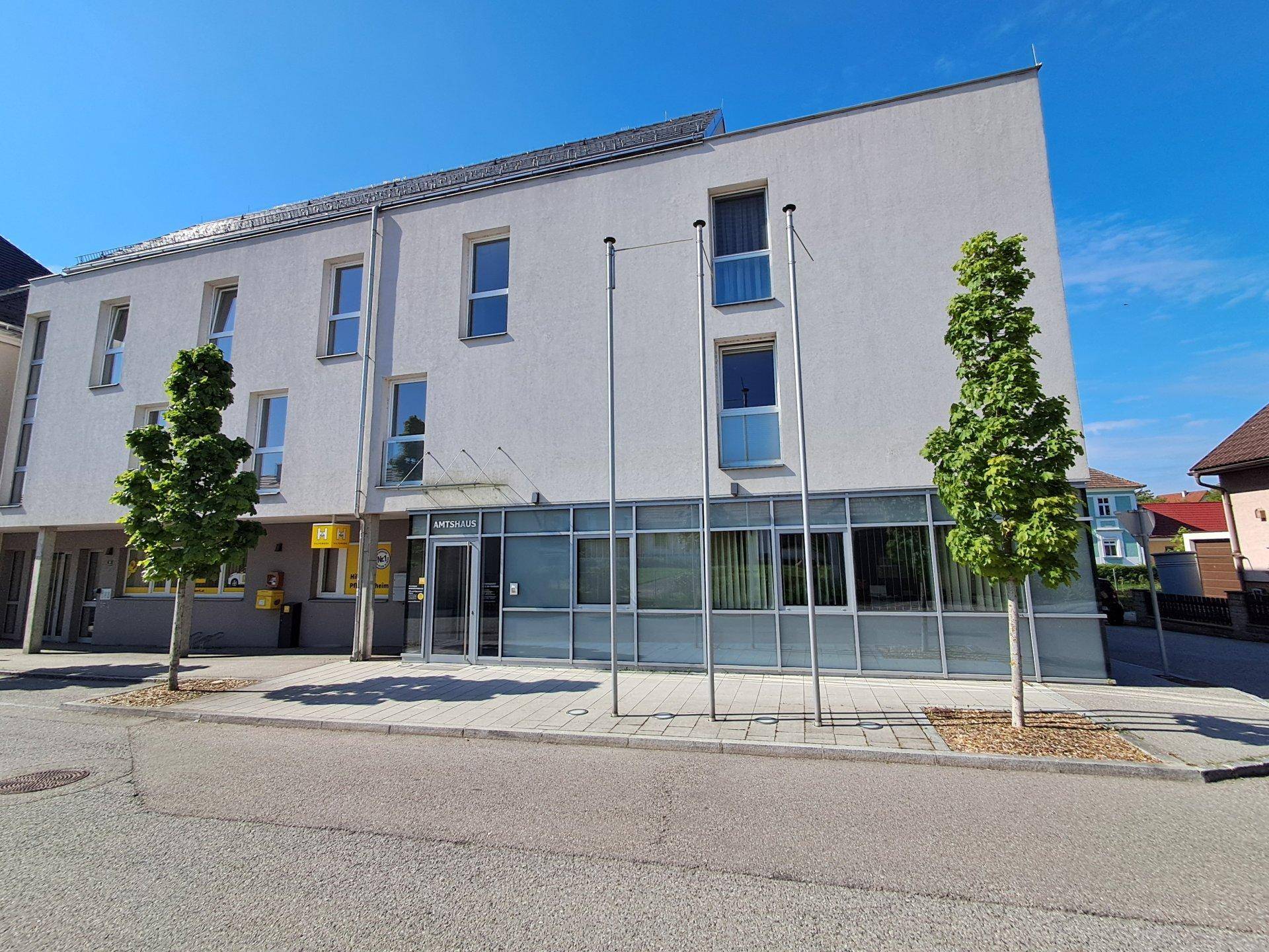 Modernes Gebäude mit weißer Fassade und großen Glasfronten im Erdgeschoss.