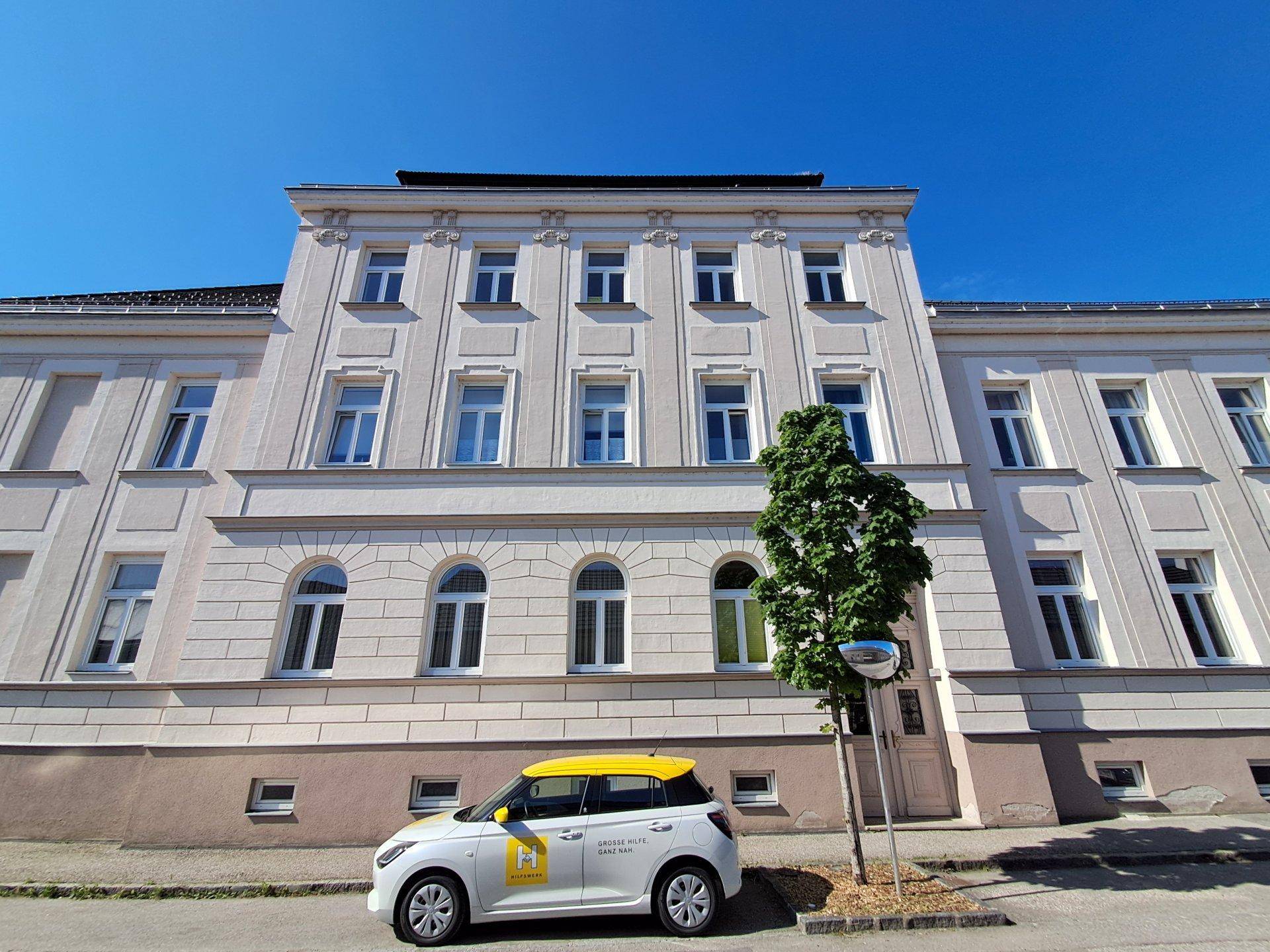 Historisches Gebäude mit heller Fassade, weißen Fenstern und architektonischen Details.