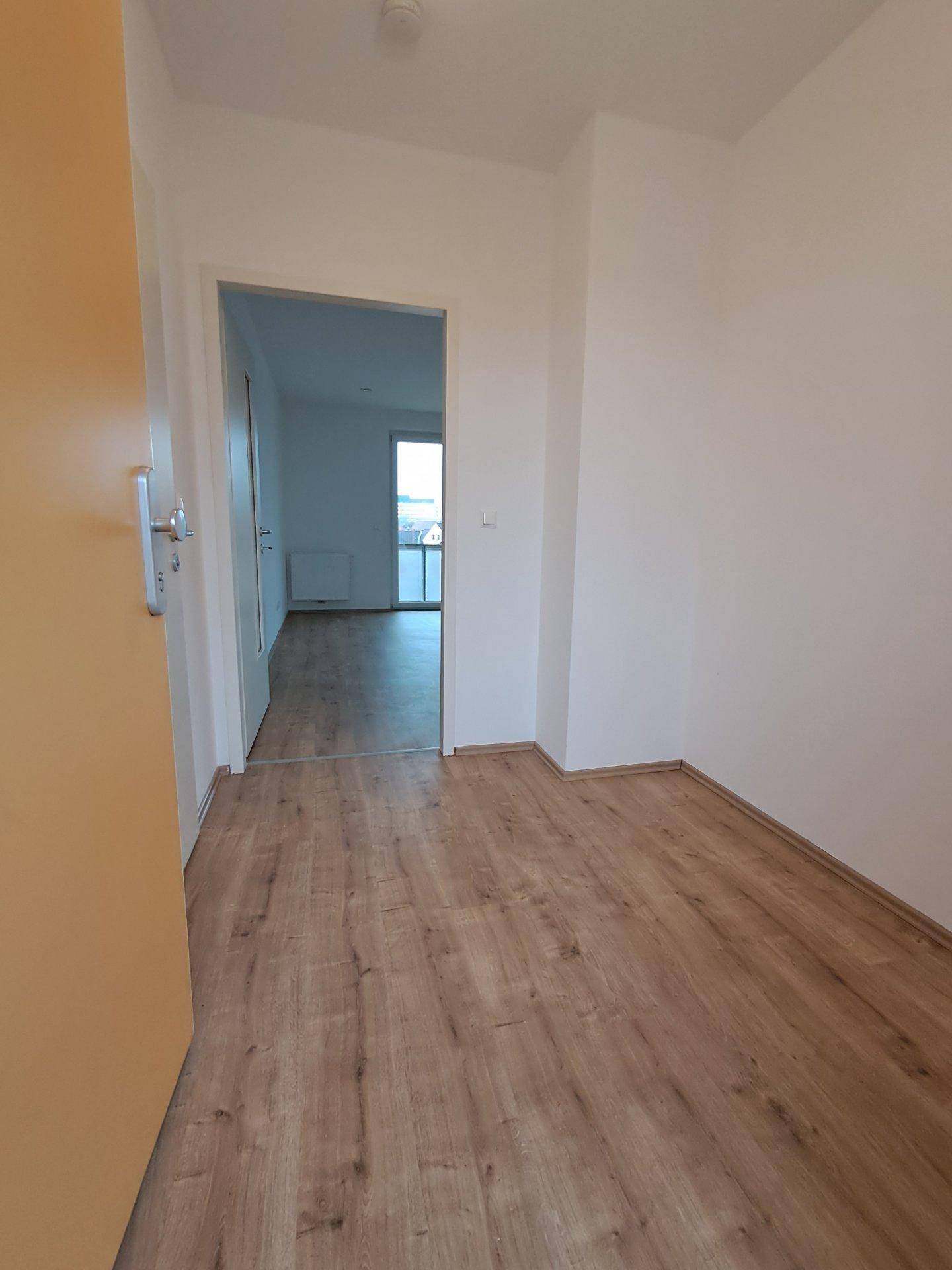 Heller Flur mit Laminatboden und weiß gestrichenen Wänden, der zu weiteren Räumen führt.