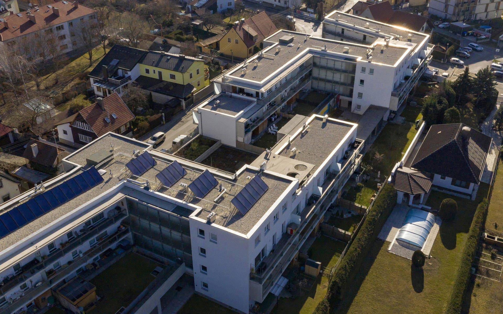 Luftaufnahme einer modernen Wohnanlage mit Flachdächern, Solaranlagen und umliegenden Grünflächen.