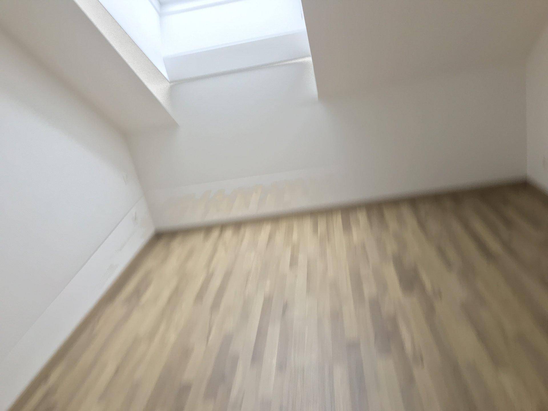 Heller Innenraum mit Holzfußboden und Dachfenster, jedoch unscharf aufgenommen.