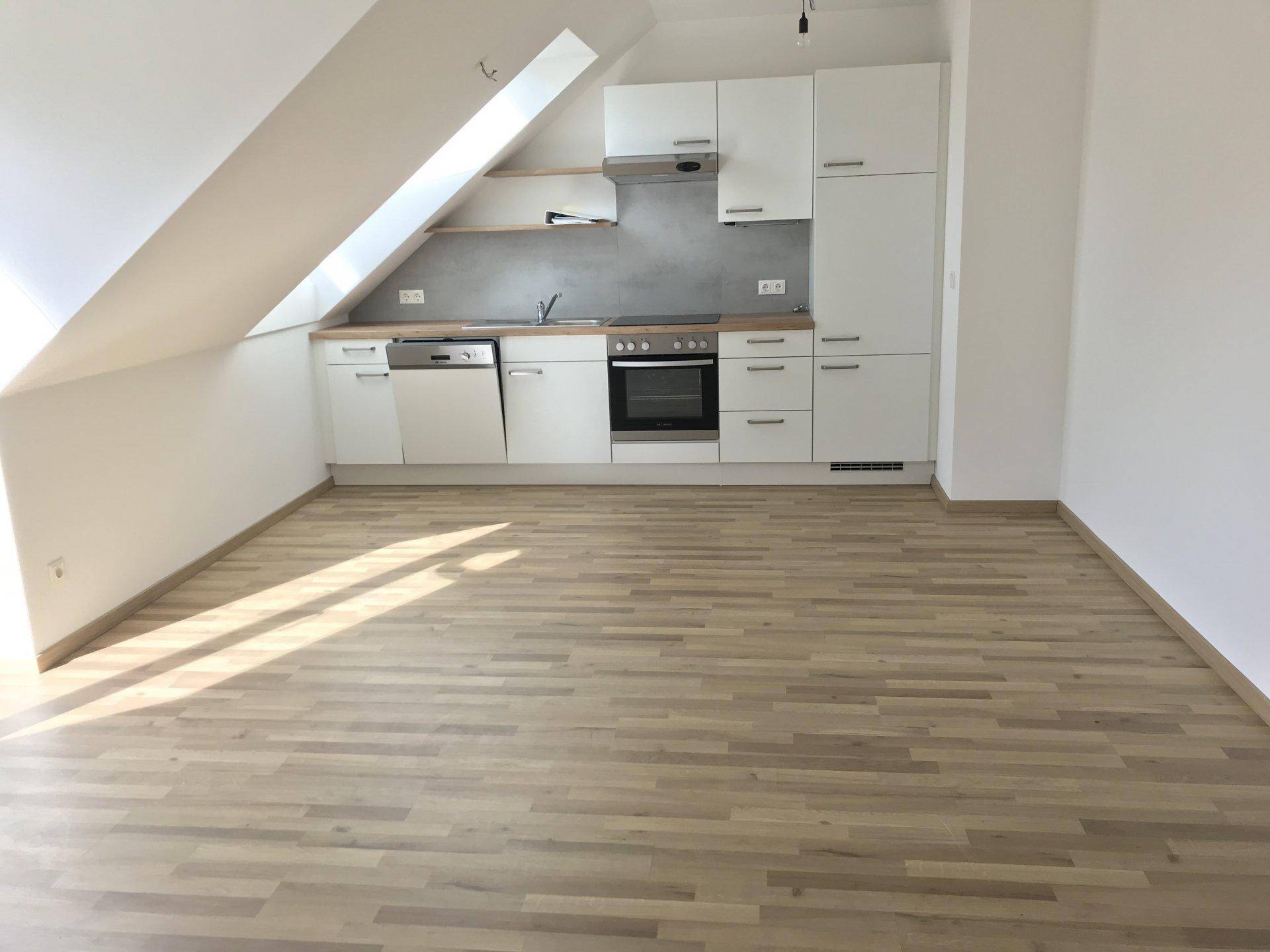 Moderne Küchenzeile mit weißen Schränken und Holzfußboden unter einer Dachschräge.