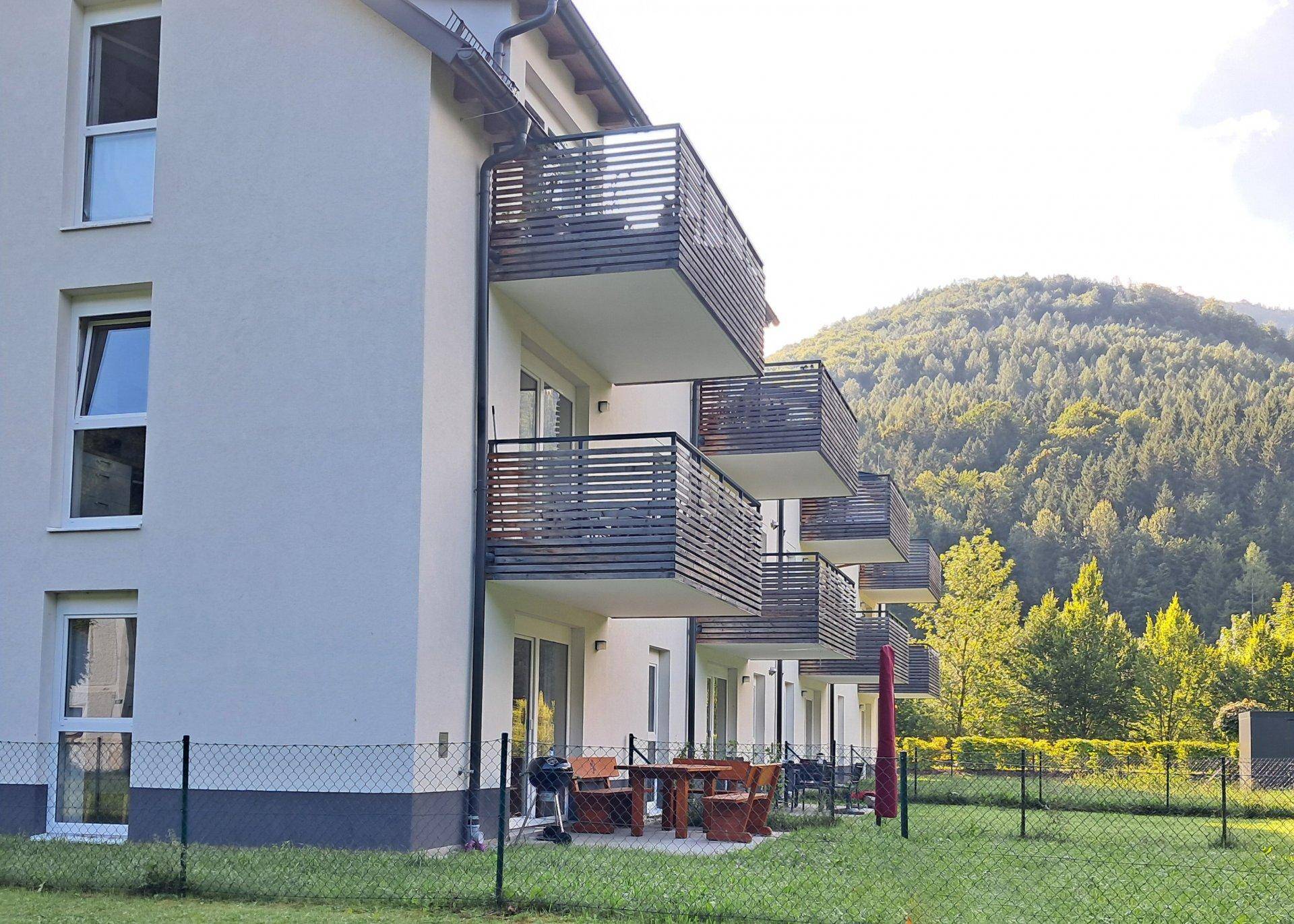 Erdgeschoss-Terrassen mit Sitzgelegenheiten und Balkone mit Blick auf die bewaldeten Hügel.