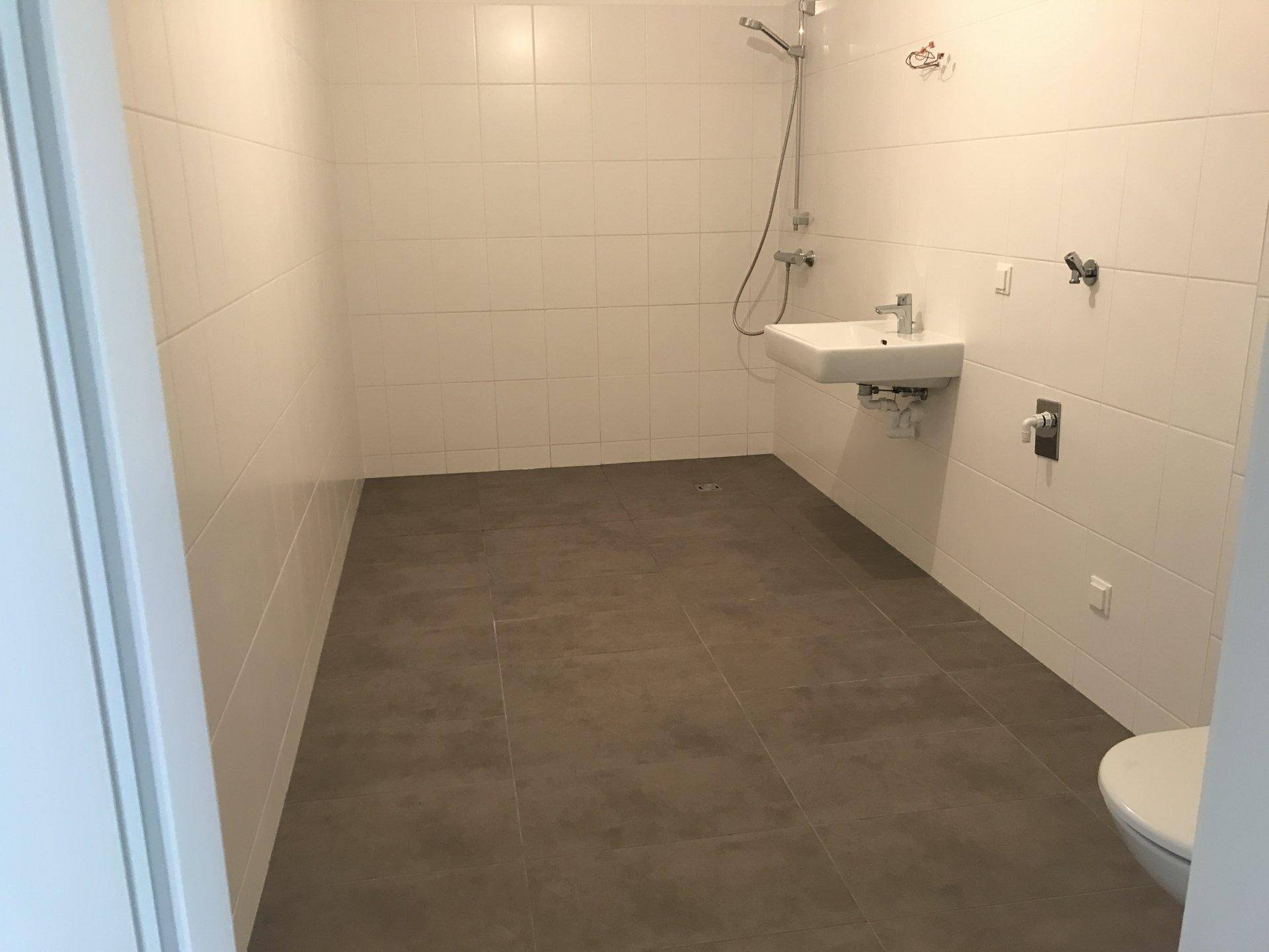Modernes Badezimmer mit weißen Wandfliesen, grauen Bodenfliesen, Dusche und wandhängendem WC.