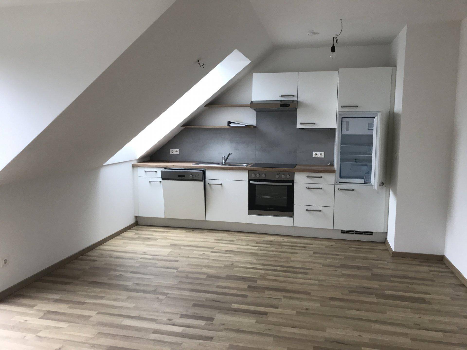 Kompakte, moderne Küchenzeile mit weißen Fronten, Kühlschrank und Holzfußboden im Dachgeschoss.