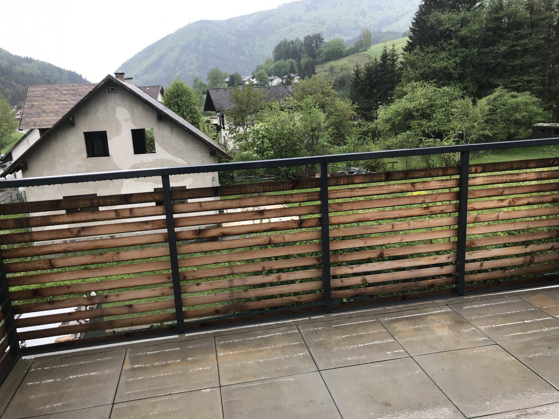 Balkon mit Fliesenboden und Holzgeländer, bietet einen weiten Blick auf die bewaldete Umgebung.
