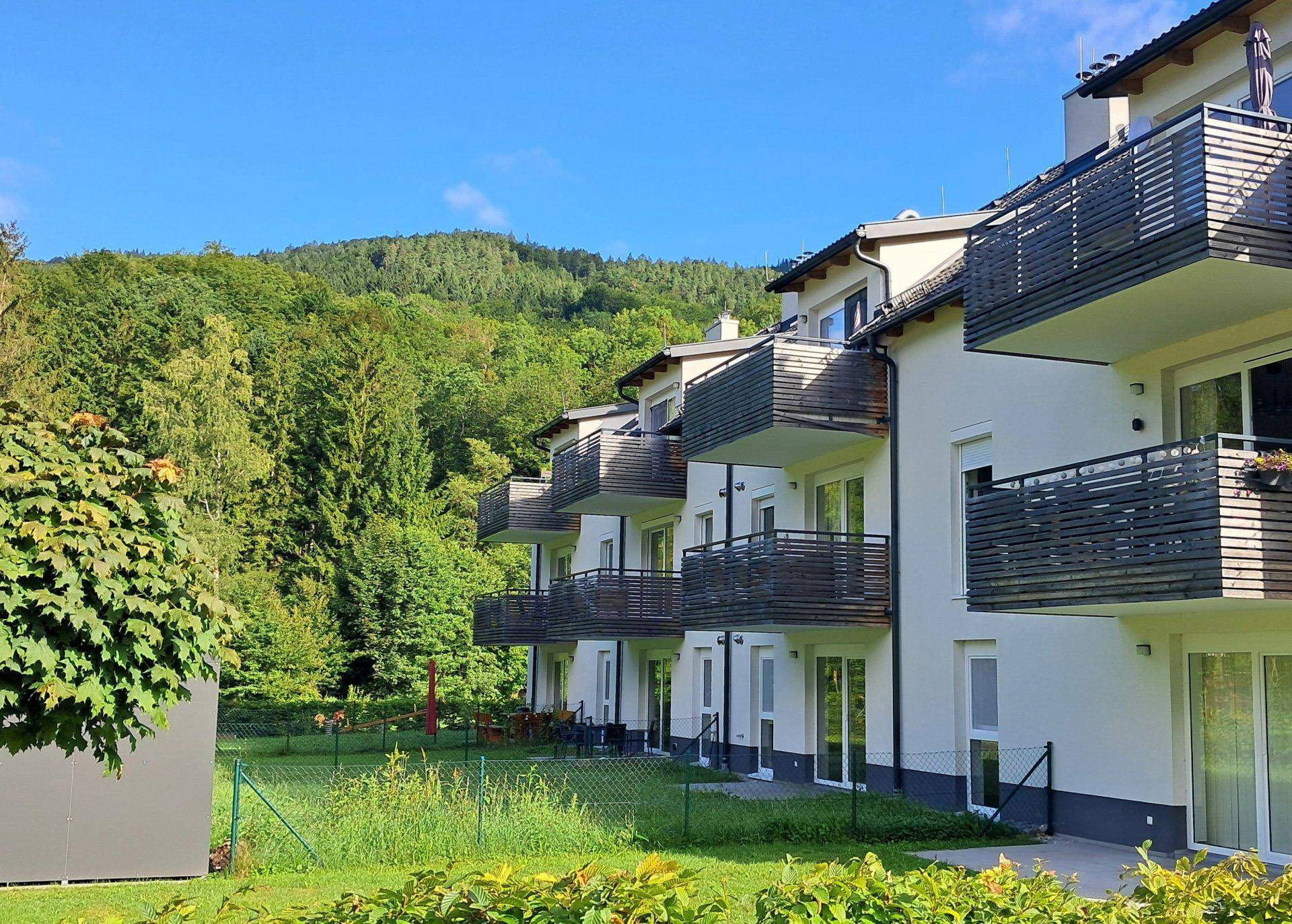 Wohngebäude mit mehreren Balkonen und umgebender Natur, eingebettet in eine grüne Landschaft.