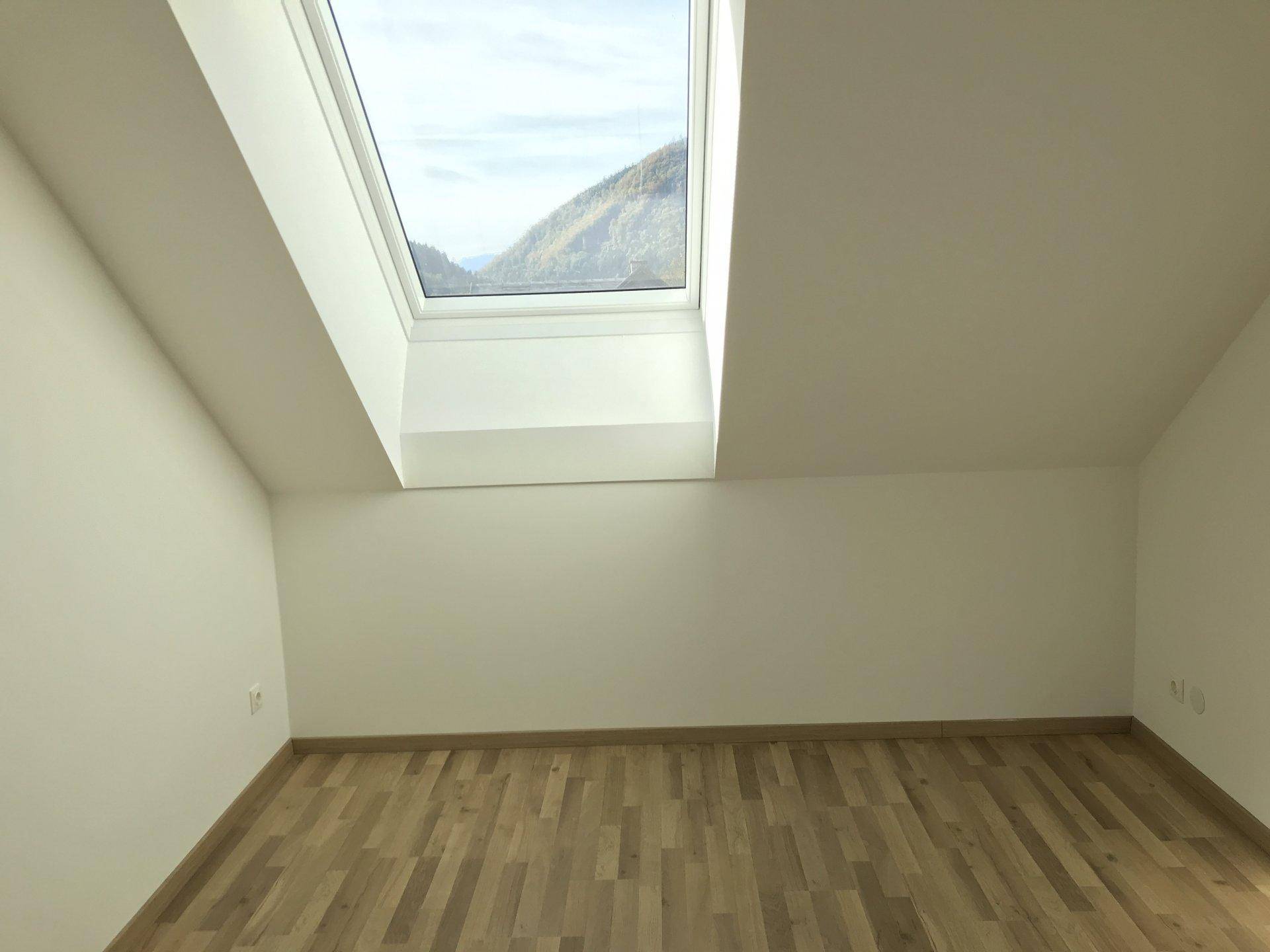 Heller Raum mit Holzfußboden und Dachfenster, das einen malerischen Bergblick bietet.