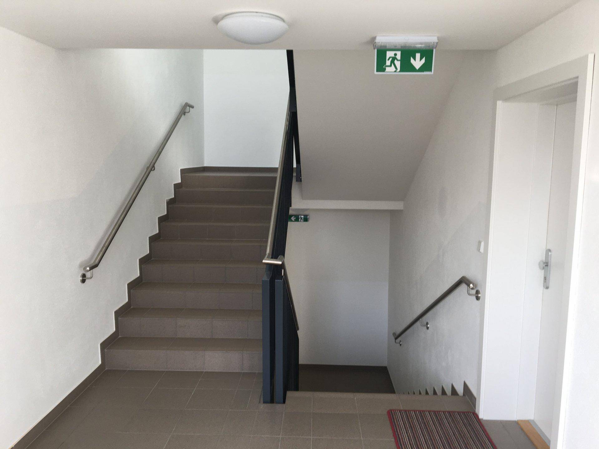 Helles Treppenhaus mit Fliesenboden und Handläufen, das die Stockwerke verbindet.
