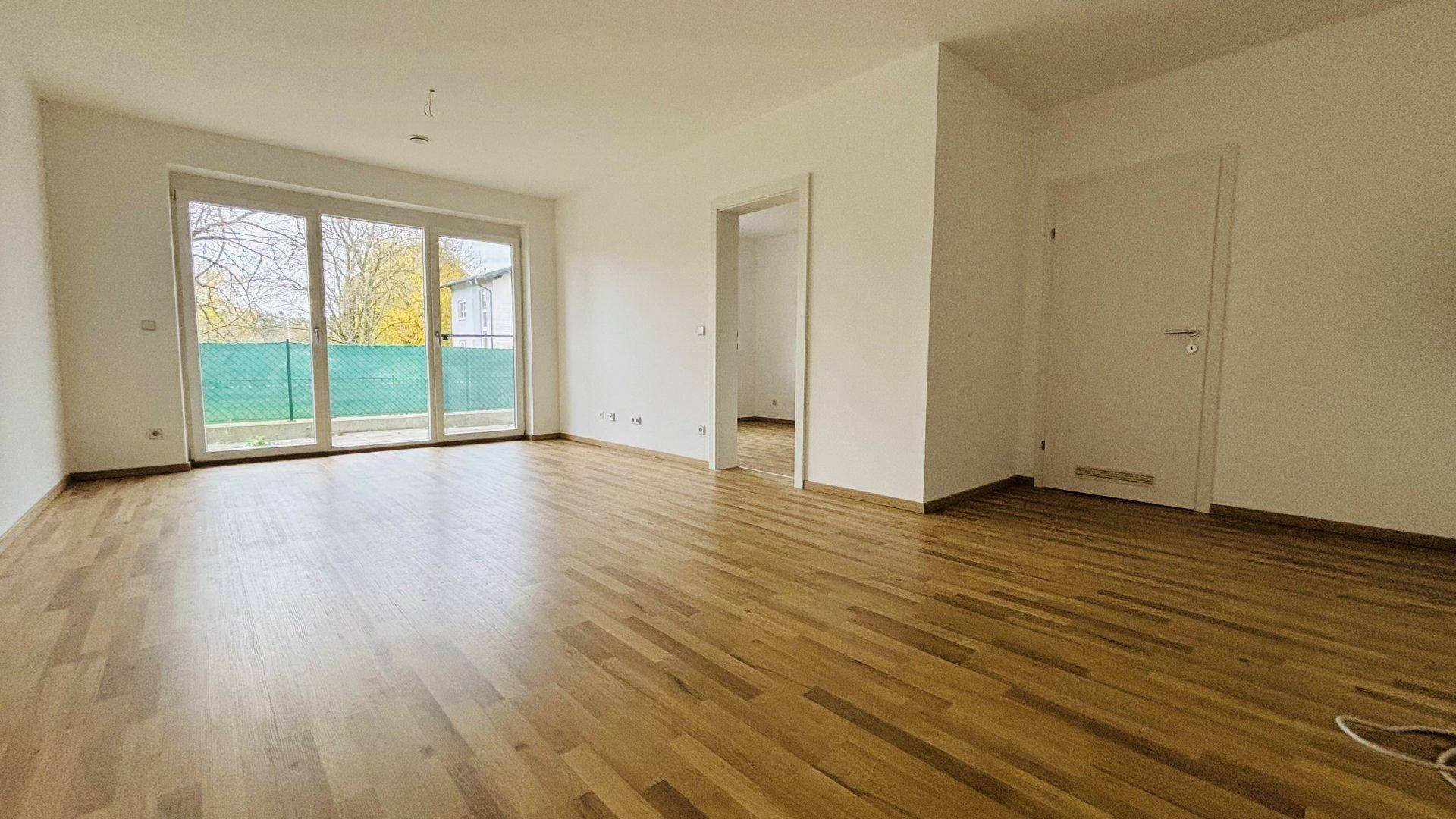Geräumiges Wohnzimmer mit hellem Parkettboden und Zugang zu einem Balkon oder einer Terrasse.