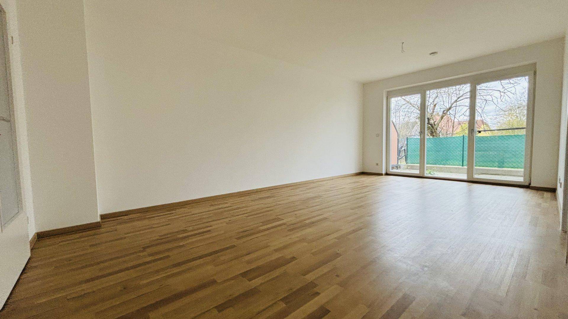 Lichtdurchflutetes Wohnzimmer mit Parkettboden und großen Schiebetüren zum Außenbereich.