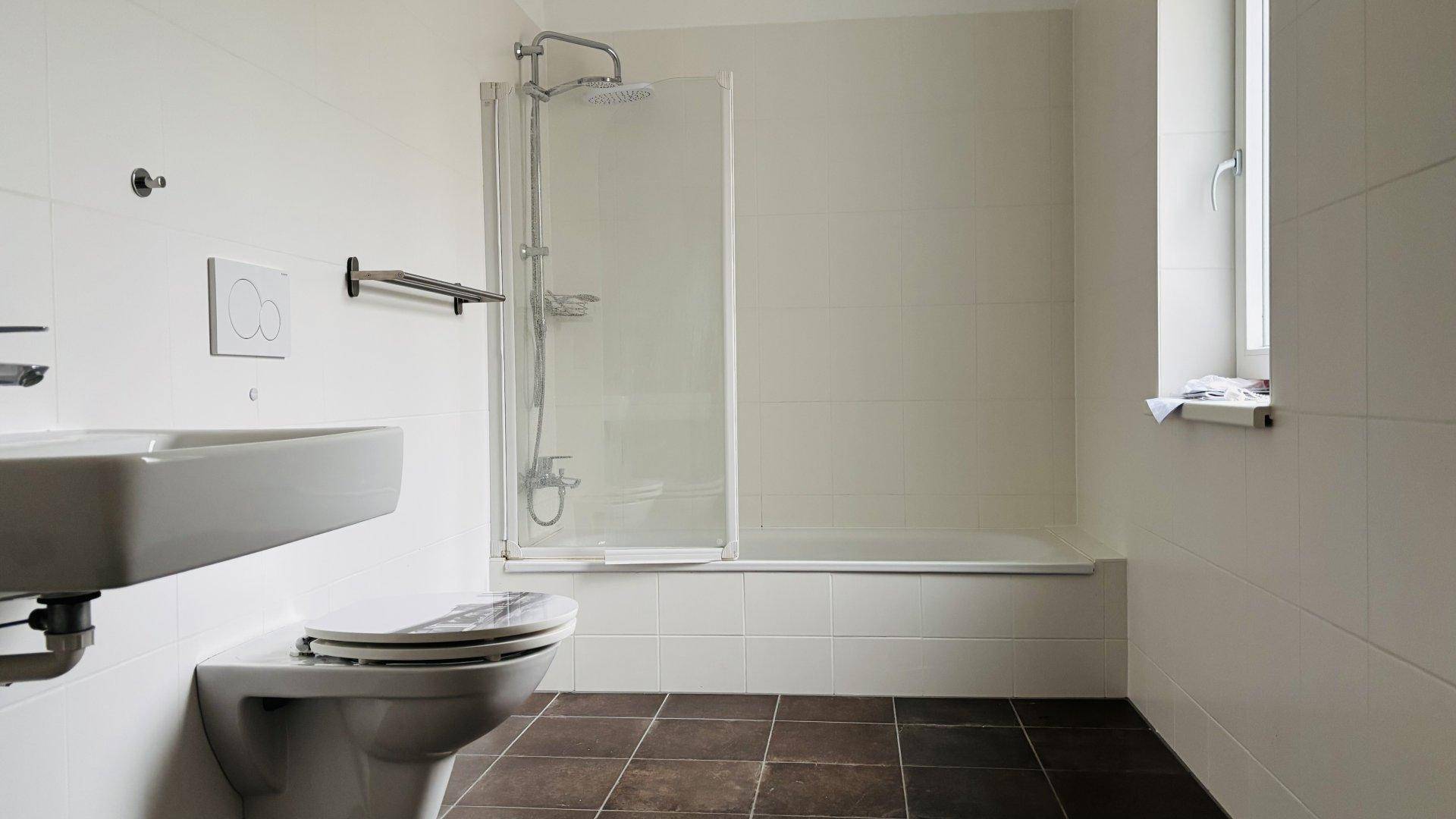 Modernes Badezimmer mit Badewanne, Dusche, WC und Fenster für natürliche Belüftung.