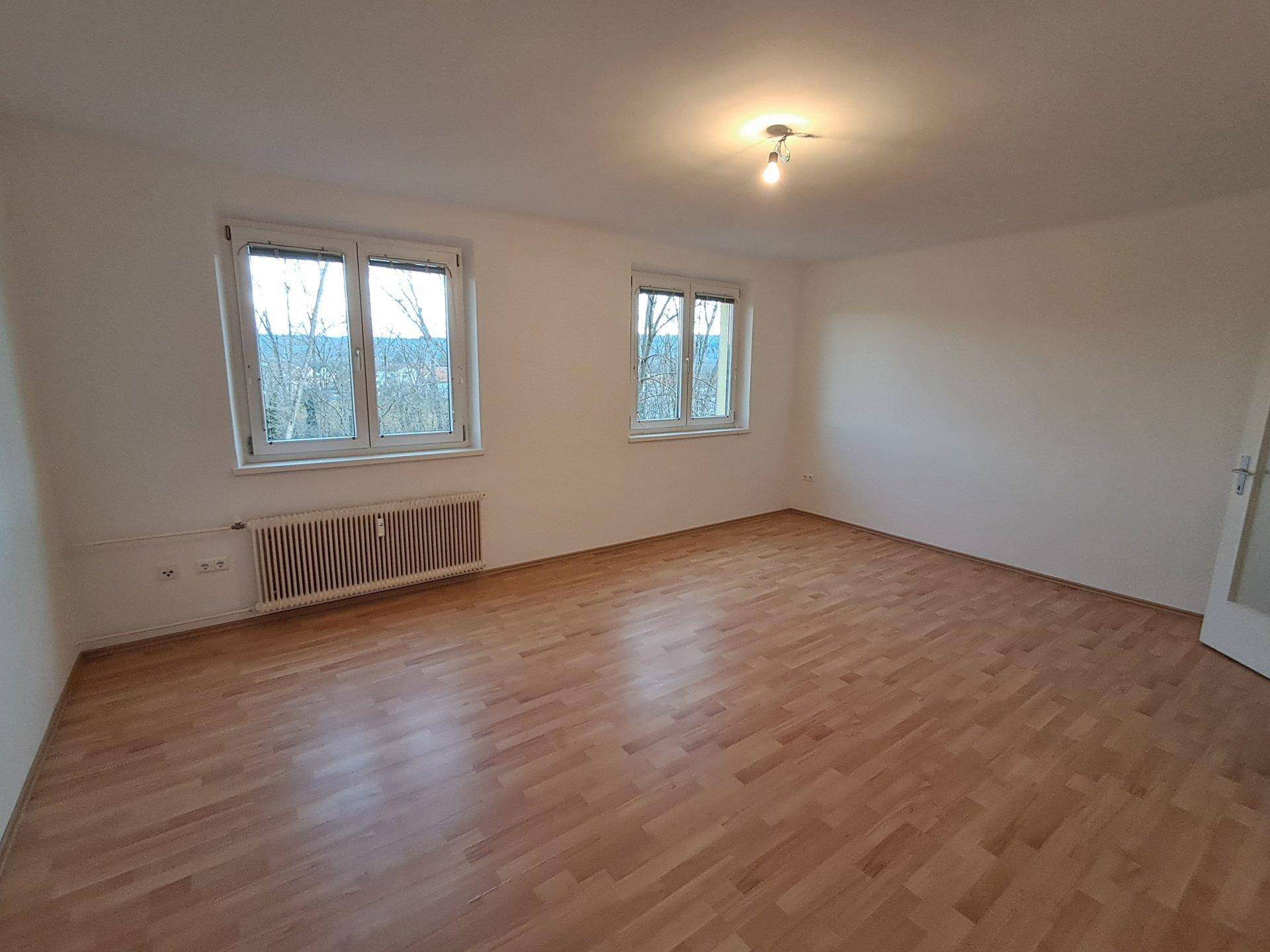 Geräumiges, helles Zimmer mit Laminatboden und zwei großen Fenstern.