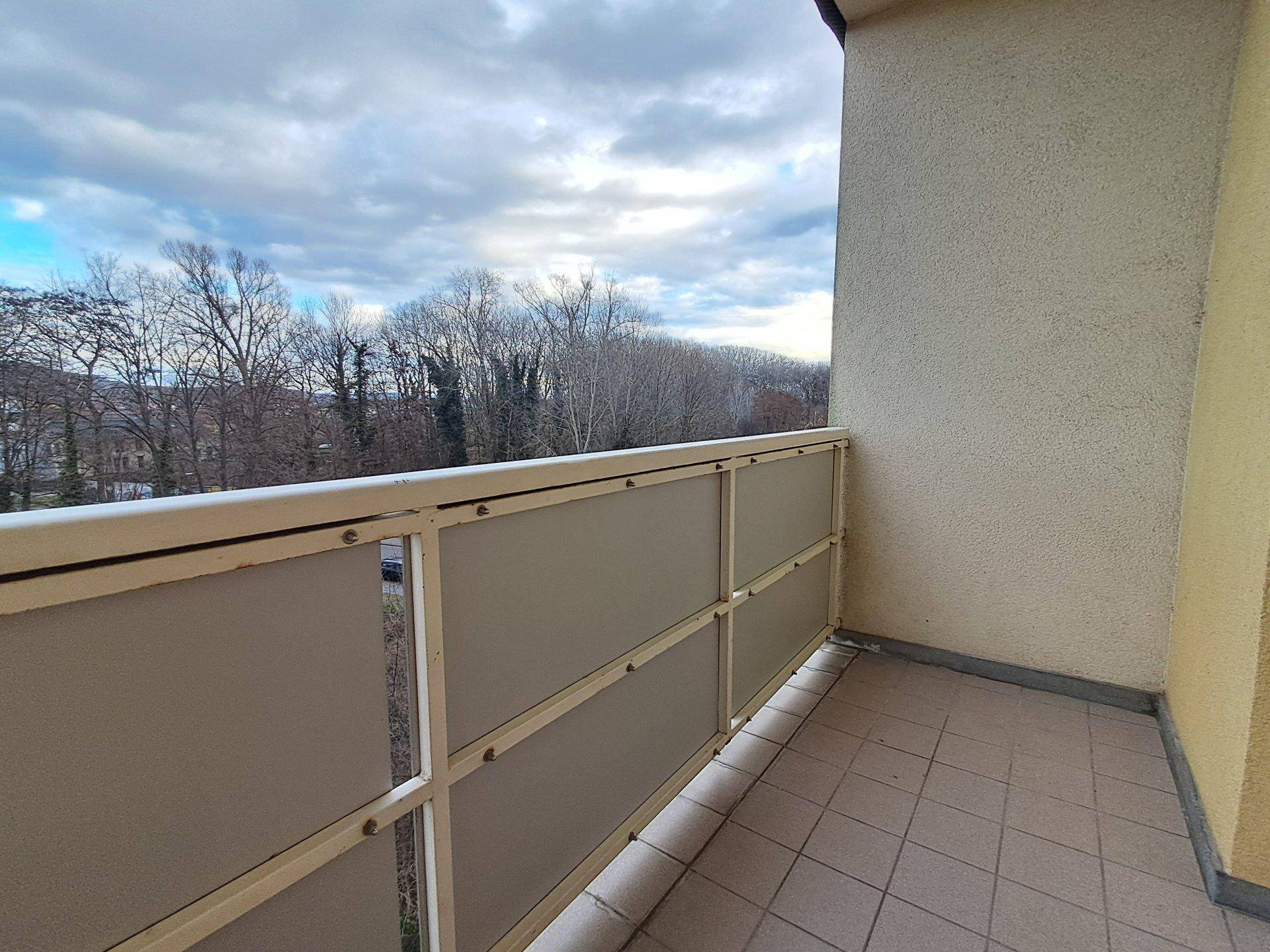 Balkon mit Fliesenboden und einer Brüstung, die einen Blick ins Grüne ermöglicht.