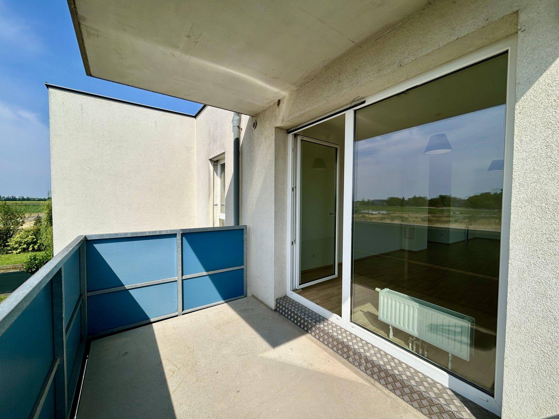 Balkon mit blauer Brüstung und großer Glasschiebetür, die den Zugang zum Innenraum ermöglicht.