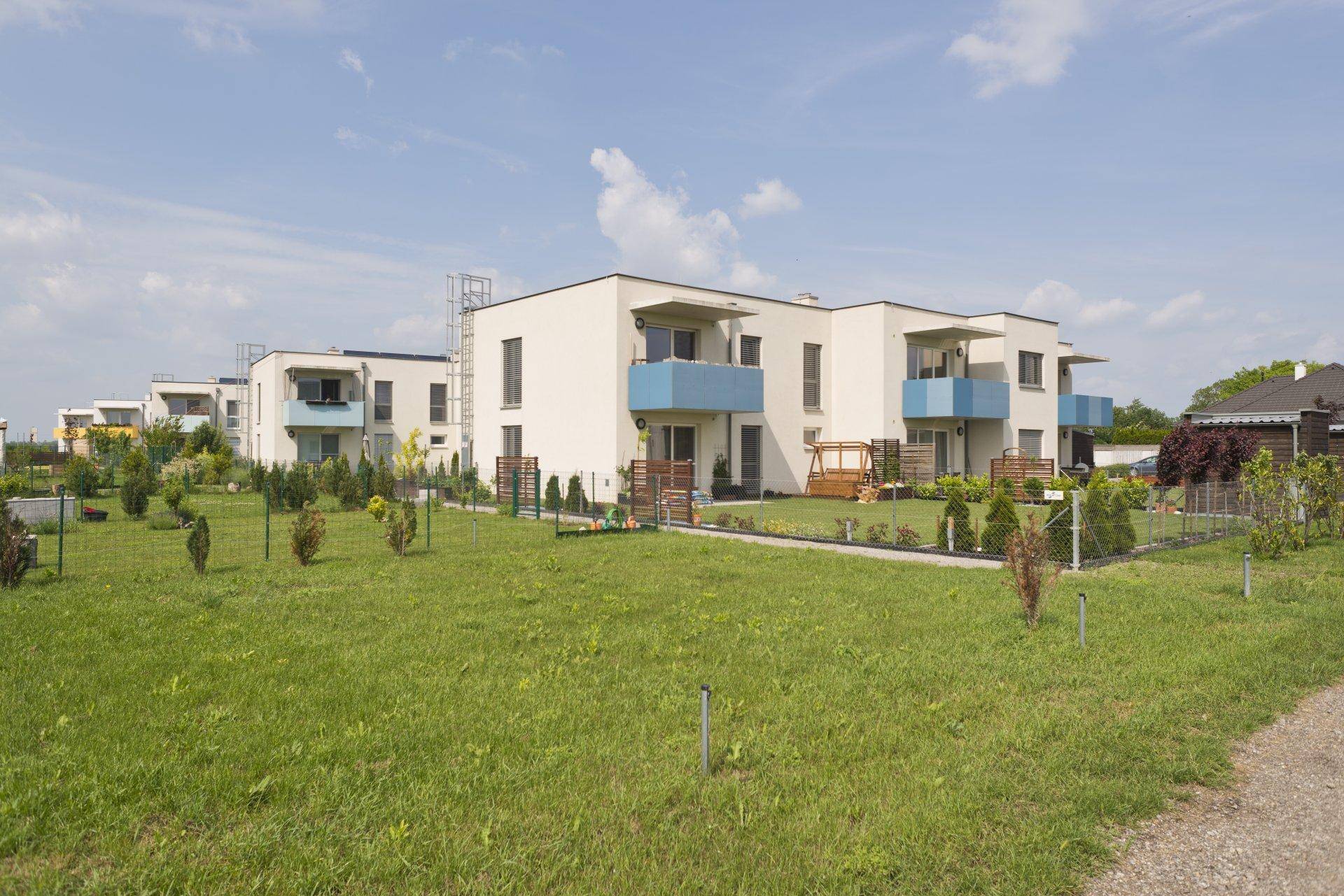 Reihe moderner Wohngebäude mit blauen Balkonen und weitläufigen Grünflächen unter hellem Himmel.