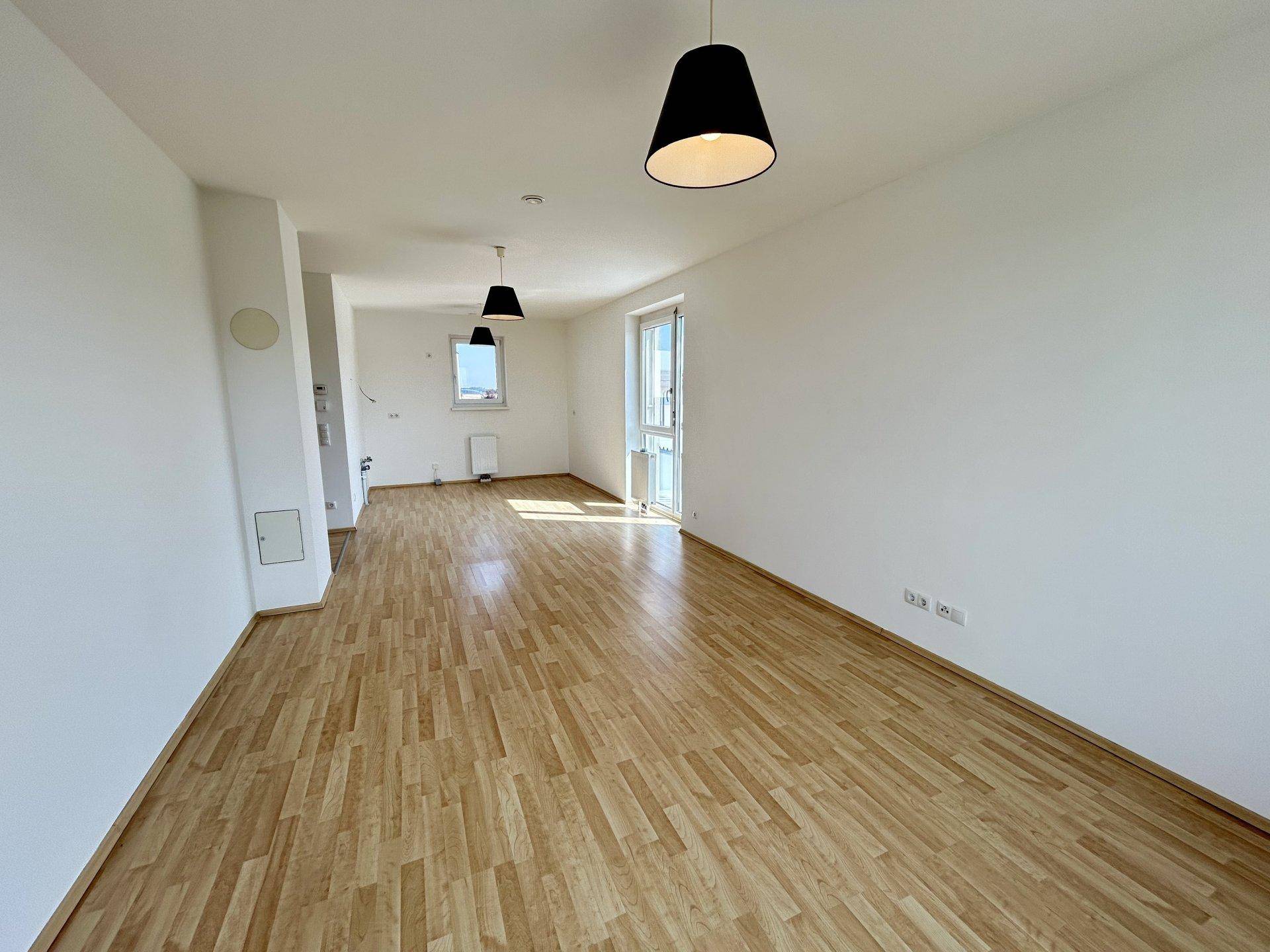 Offener Wohnbereich mit Laminatboden, weißen Wänden und viel Tageslicht durch mehrere Fenster.
