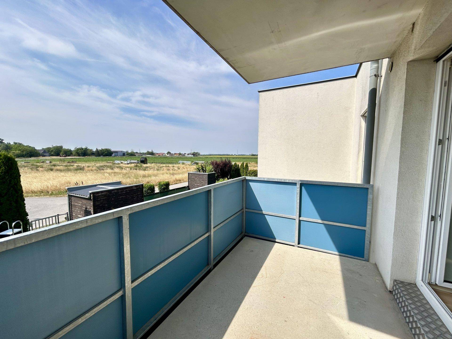 Balkon mit blauer Brüstung und weitem Blick über die umliegende Landschaft und Felder.