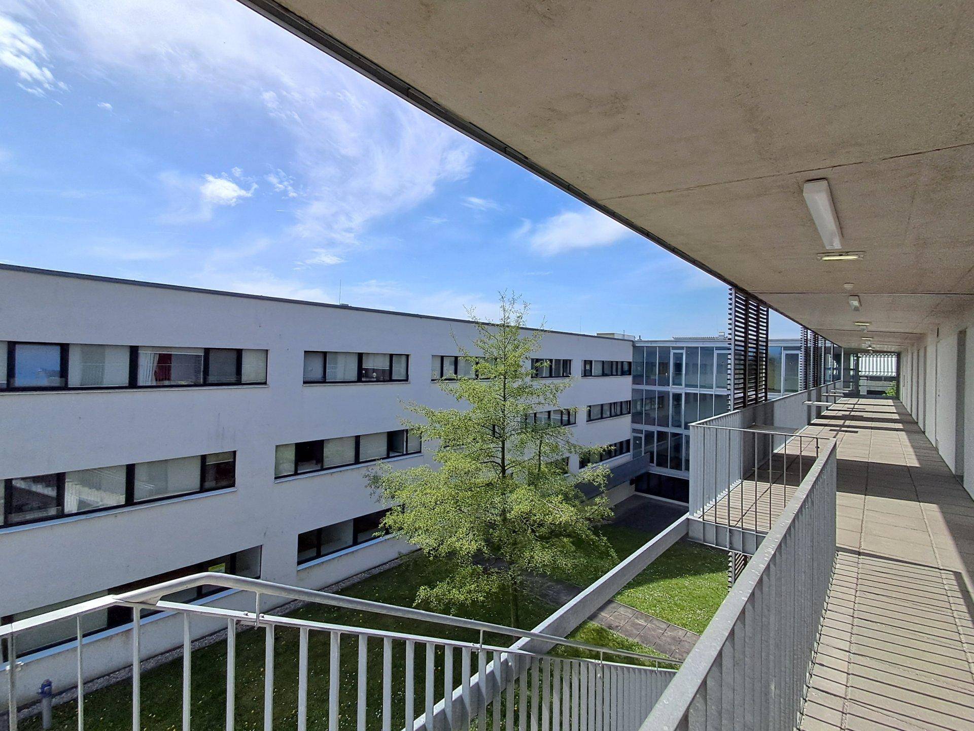 Blick von einem erhöhten Balkon auf den begrünten Innenhof des modernen Gebäudekomplexes.