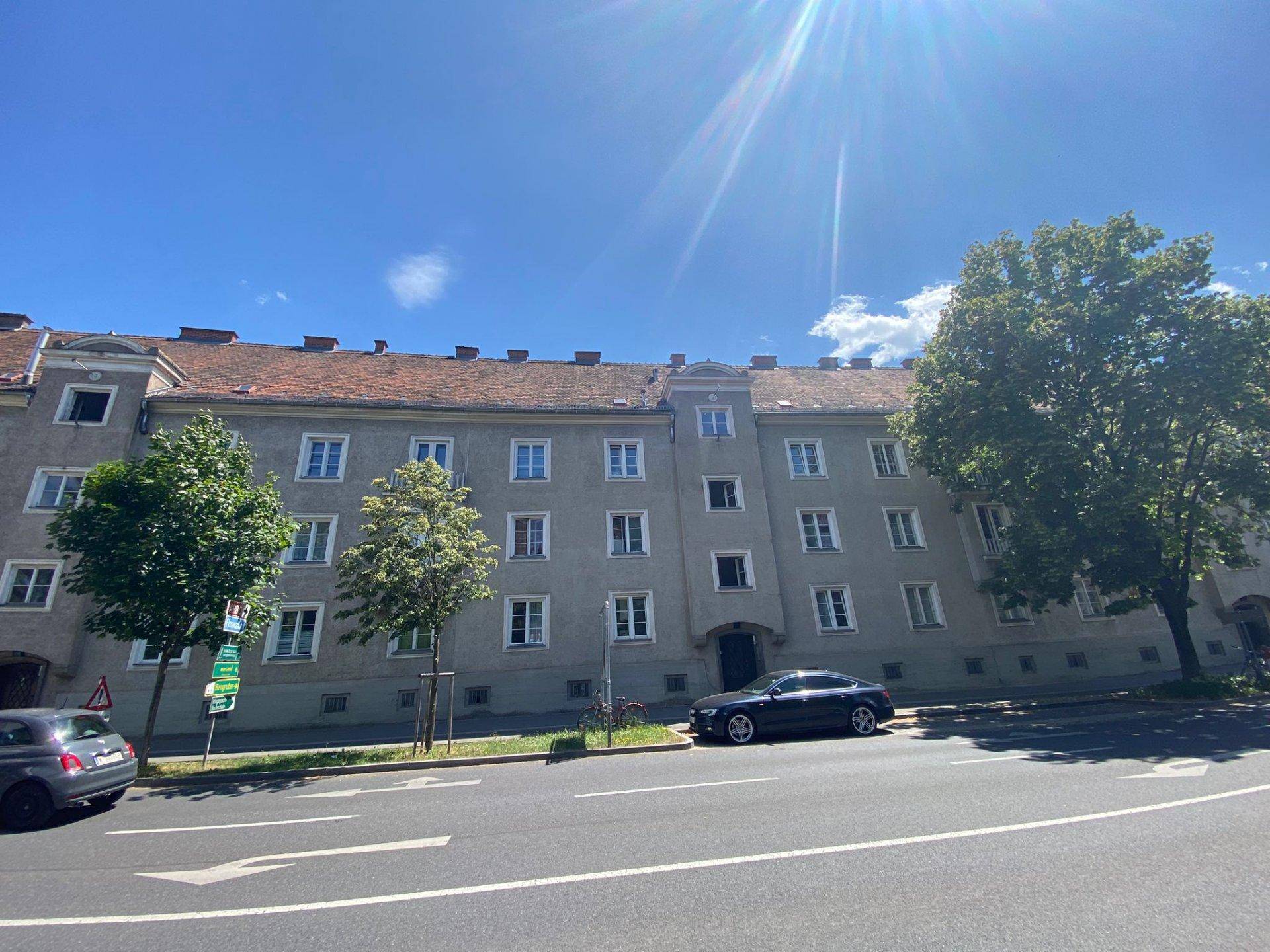 Gesamtansicht des Wohnhauses von der Straße aus mit parkenden Autos und Bäumen.