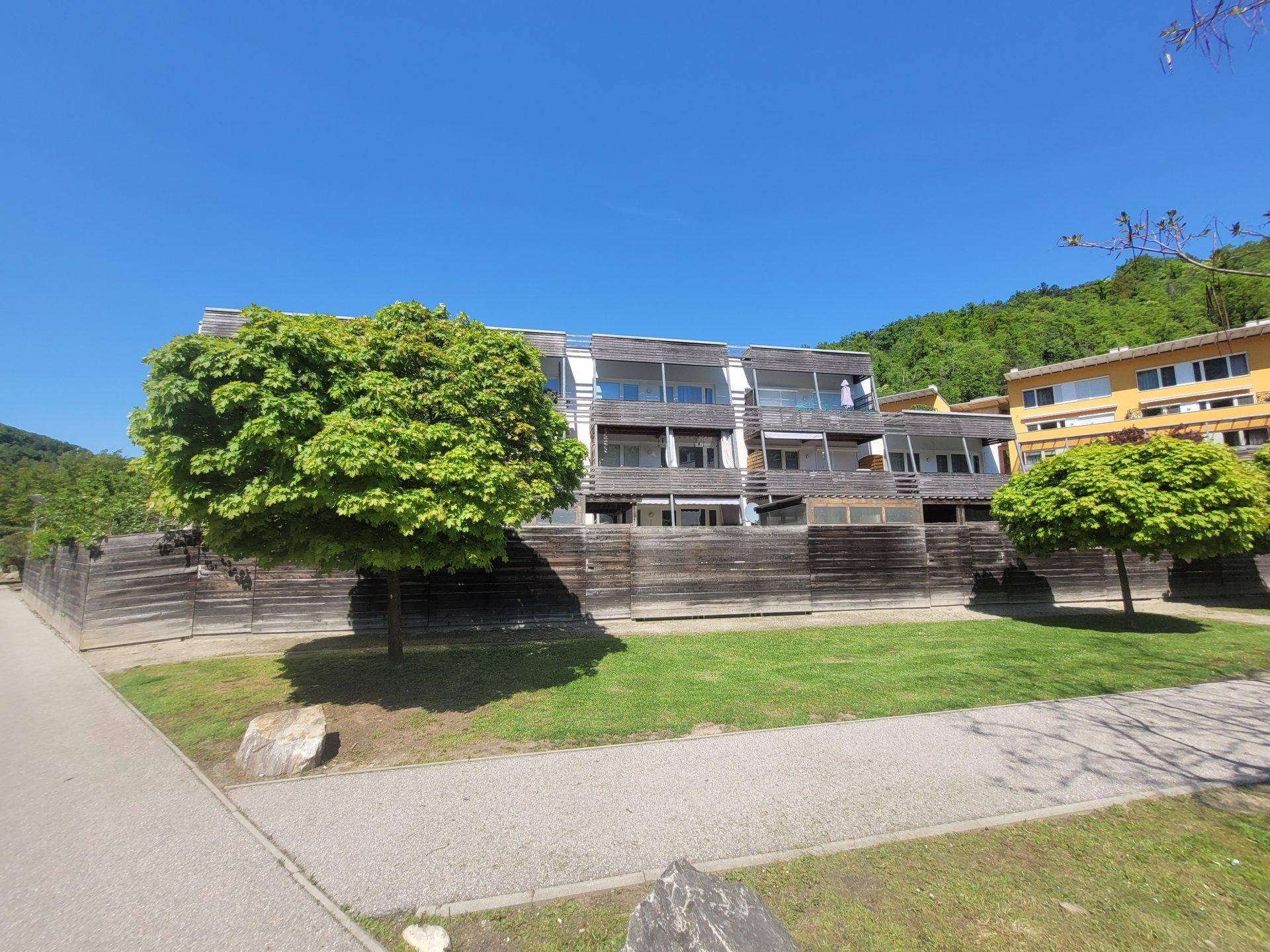 Moderne Wohngebäude mit Holzfassade und Balkonen, eingebettet in eine grüne Hügellandschaft.