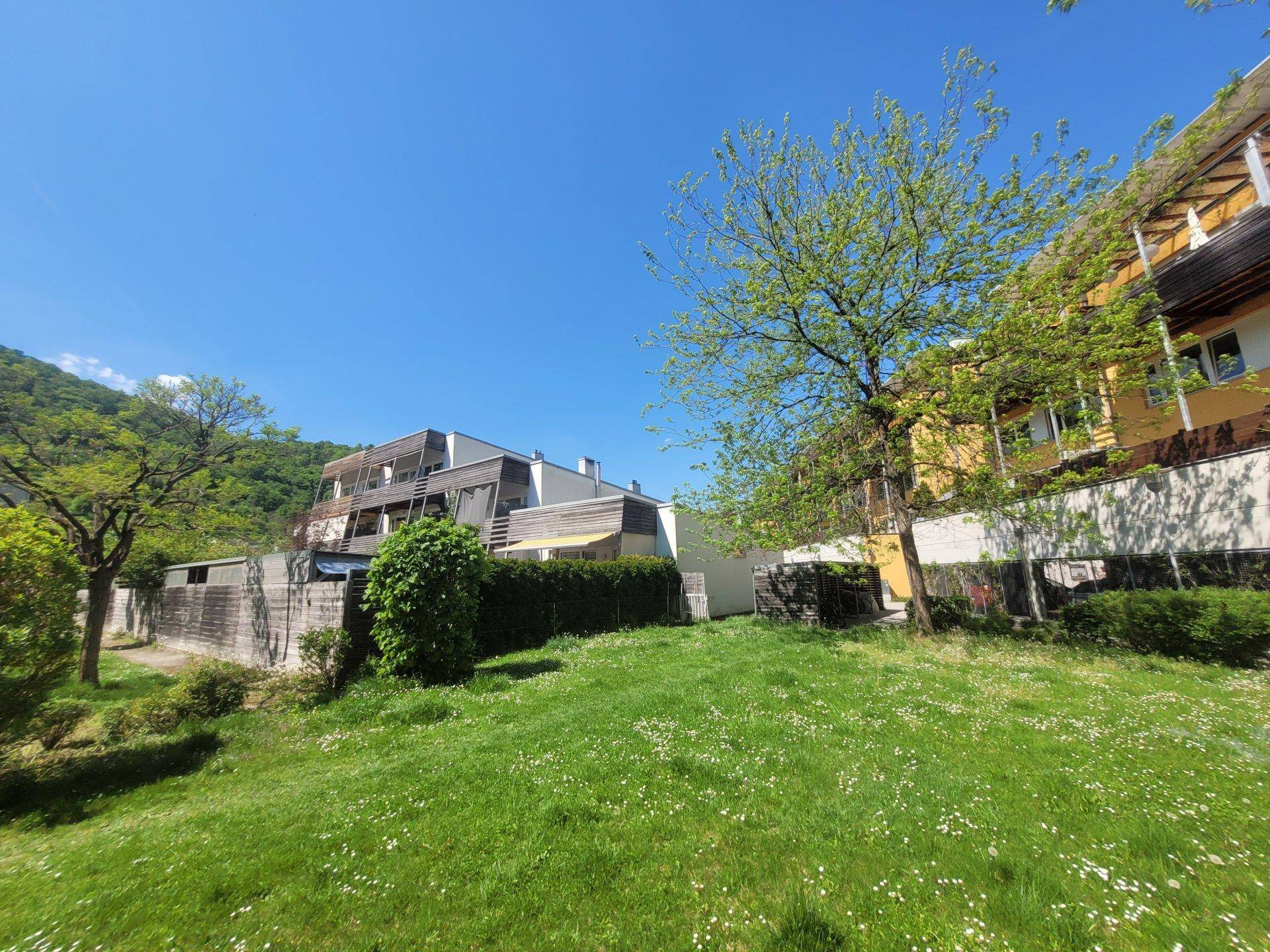 Moderne Wohngebäude mit Holzfassaden und Balkonen, umgeben von einer blühenden Wiese und Bäumen.