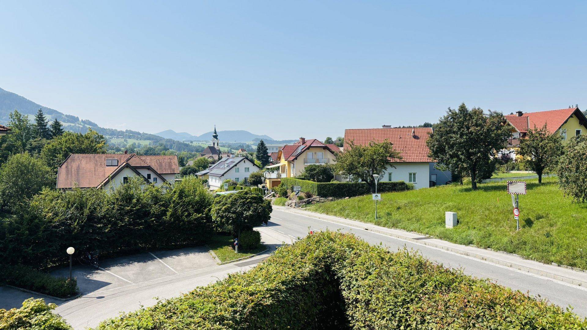 Blick über eine ruhige Wohnstraße mit Einfamilienhäusern und grüner Landschaft im Hintergrund.