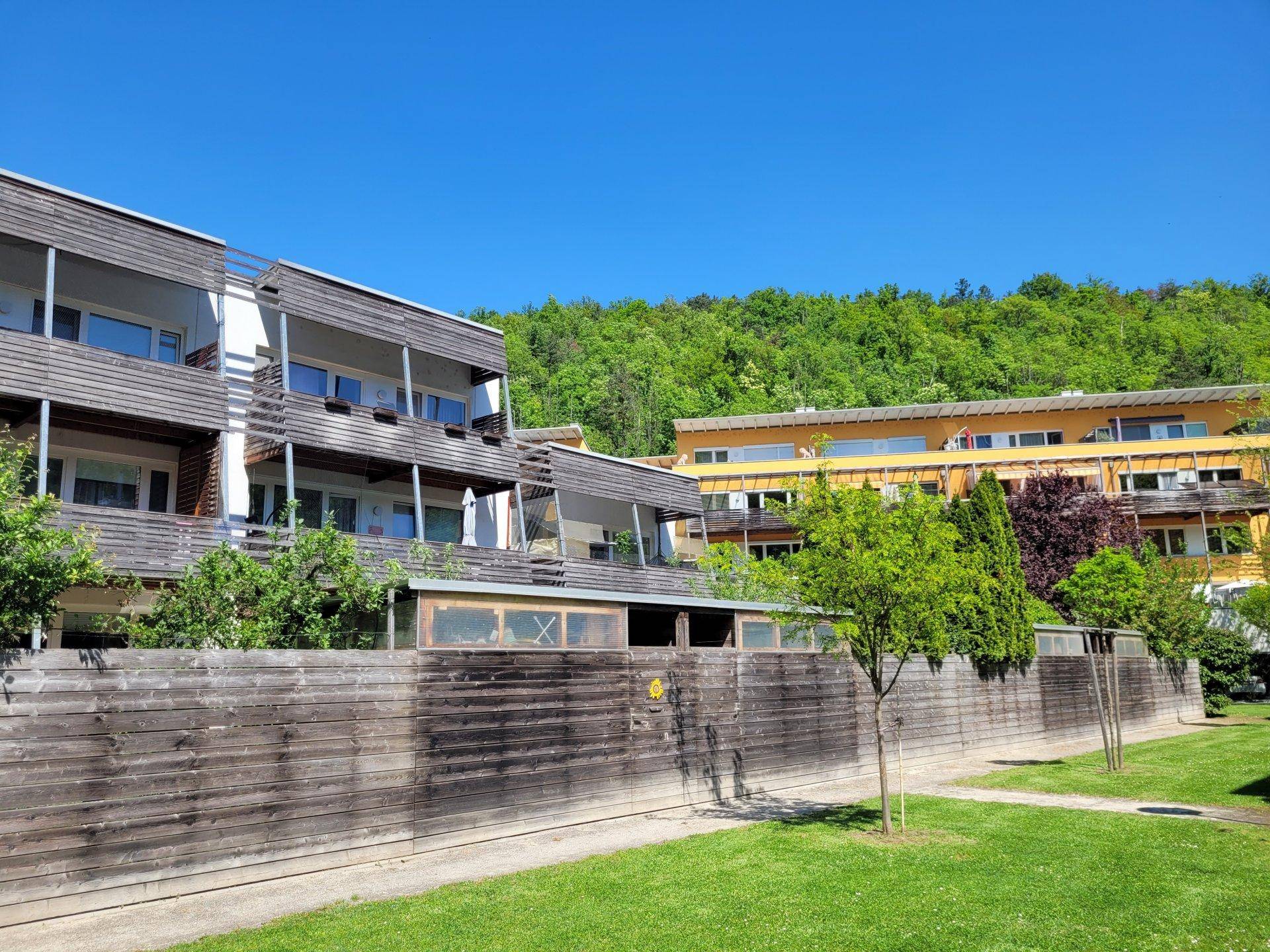 Moderne Wohngebäude mit Holzfassade und Balkonen, eingebettet in eine grüne Hügellandschaft.