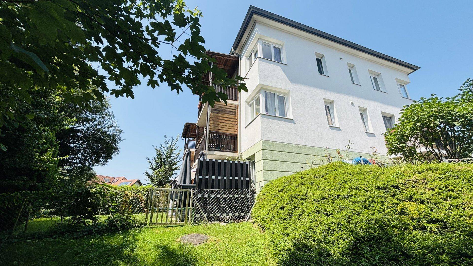 Seitenansicht des Gebäudes mit Balkonen und gepflegter Hecke im Vordergrund unter blauem Himmel.