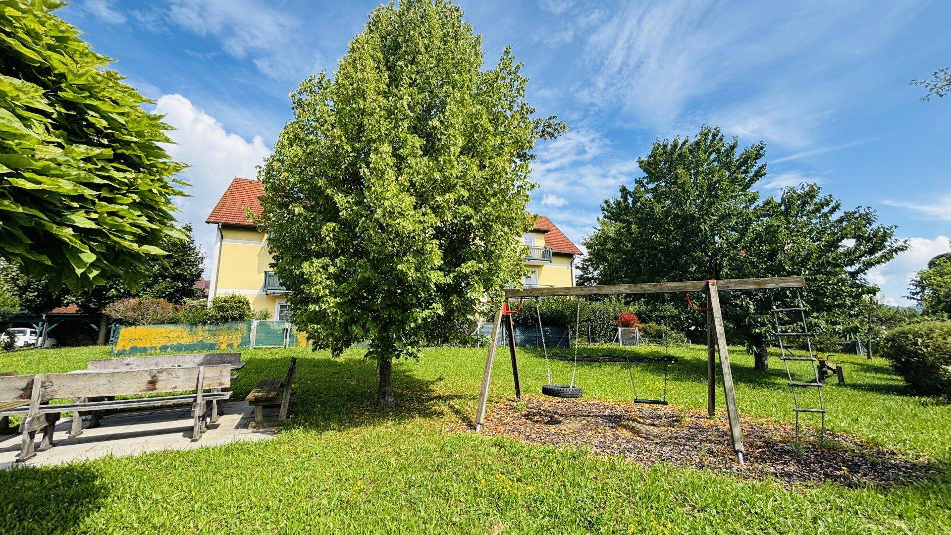 Kinderspielplatz mit Schaukel und Klettergerüst auf einer grünen Wiese vor dem Wohngebäude.