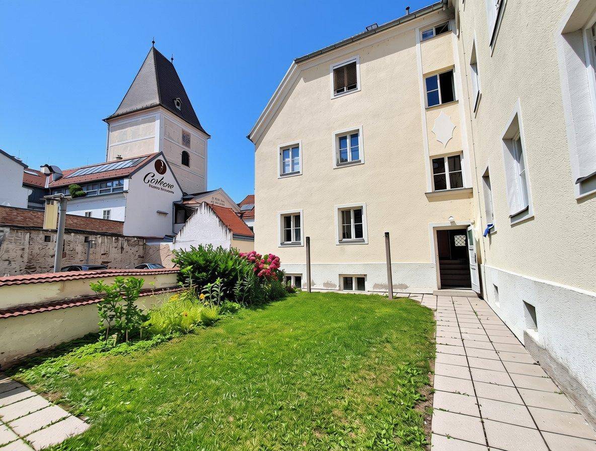 Kleiner Gartenbereich hinter dem Gebäude mit Rasenfläche und angrenzendem historischen Turm.