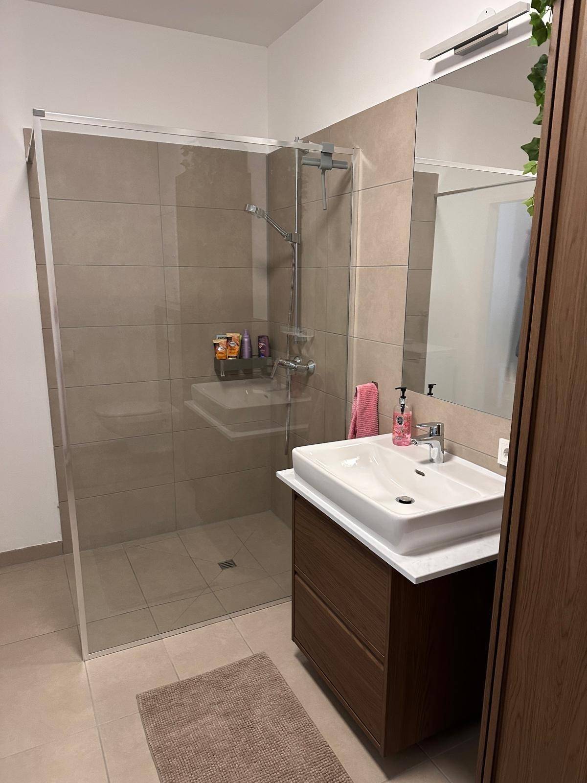 Geräumige Dusche mit Glasabtrennung und modernem Waschbeckenbereich in hellen Farben.
