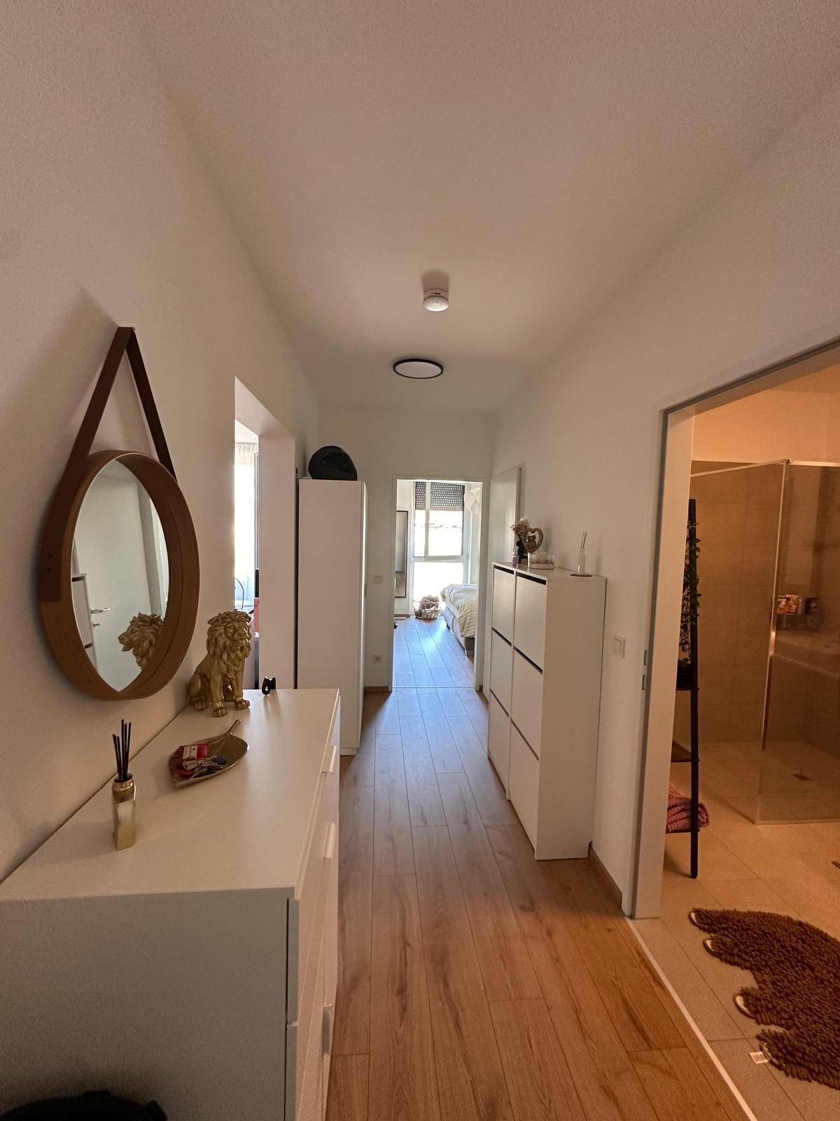 Heller Flur mit modernem Laminatboden, weißer Kommode und Zugang zu einem modernen Badezimmer.