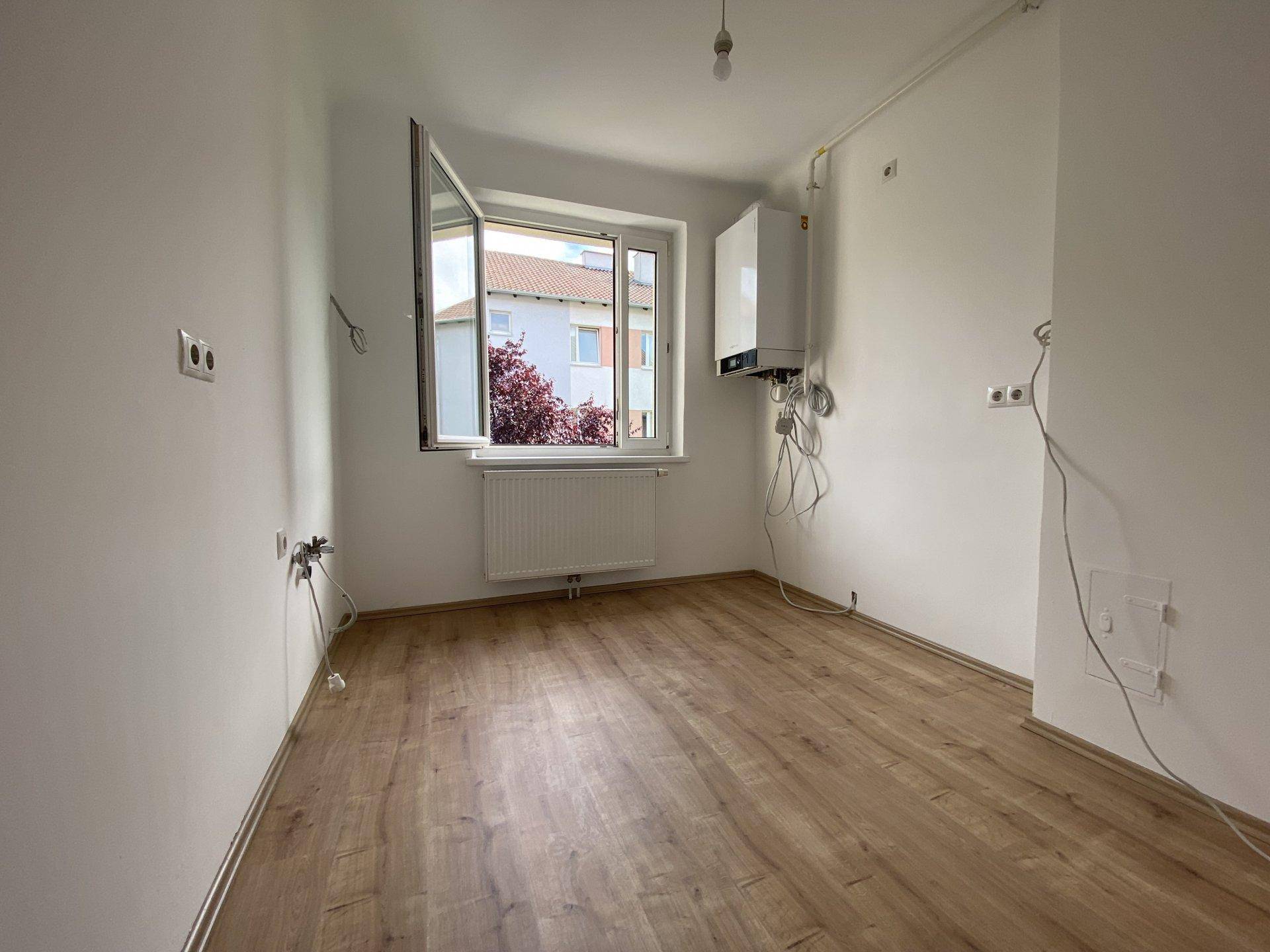 Leerer Raum mit Laminatboden, Fenster und einer Gastherme an der Wand.