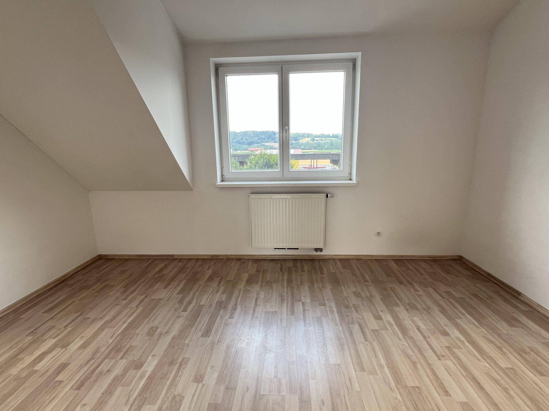 Helles Schlafzimmer mit hellem Laminatboden, weiß gestrichenen Wänden und einem Fenster mit Ausblick.
