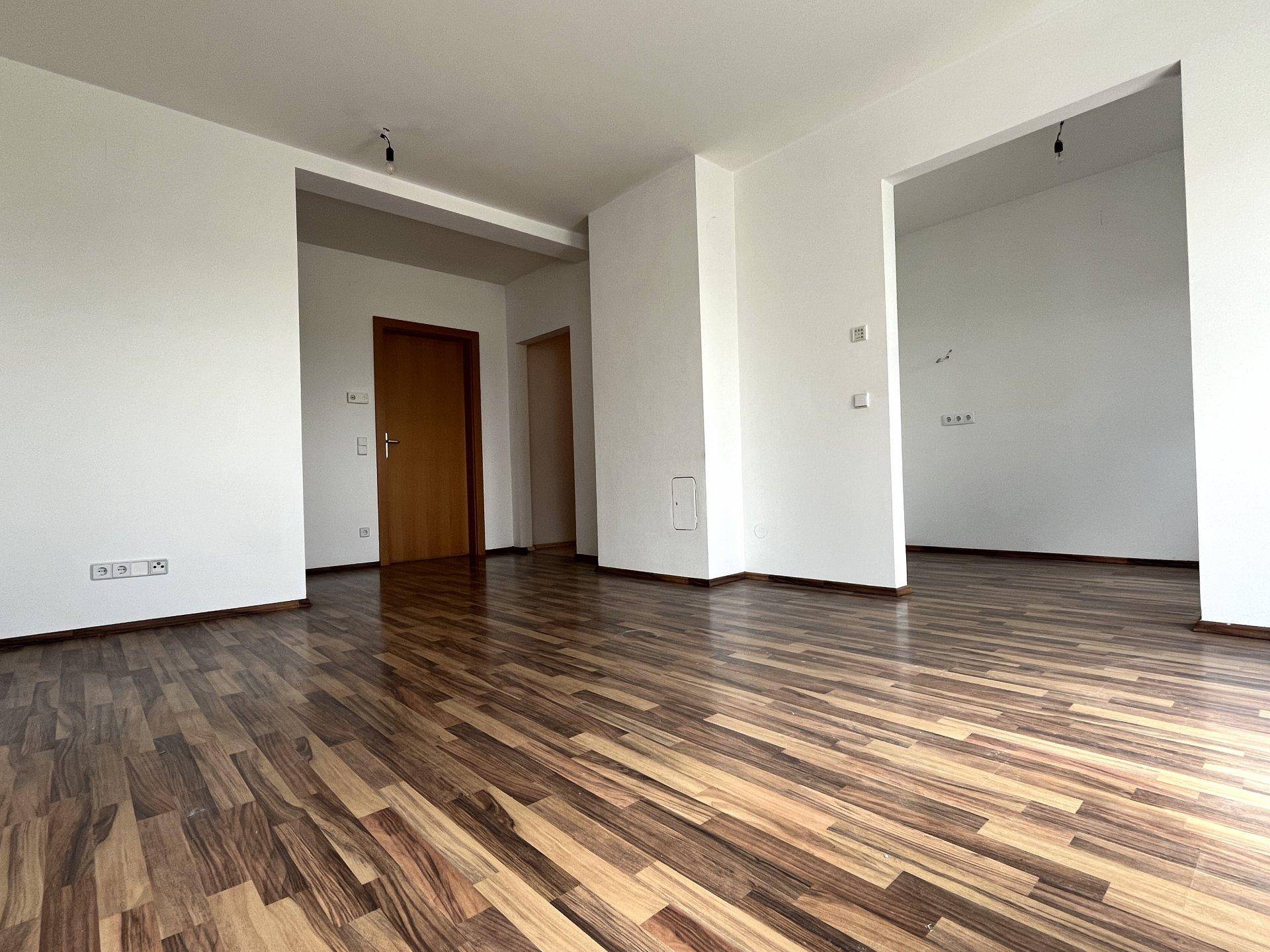 Heller Wohnraum mit dunklem Laminatboden und weiß gestrichenen Wänden, bereit zur individuellen Gestaltung.
