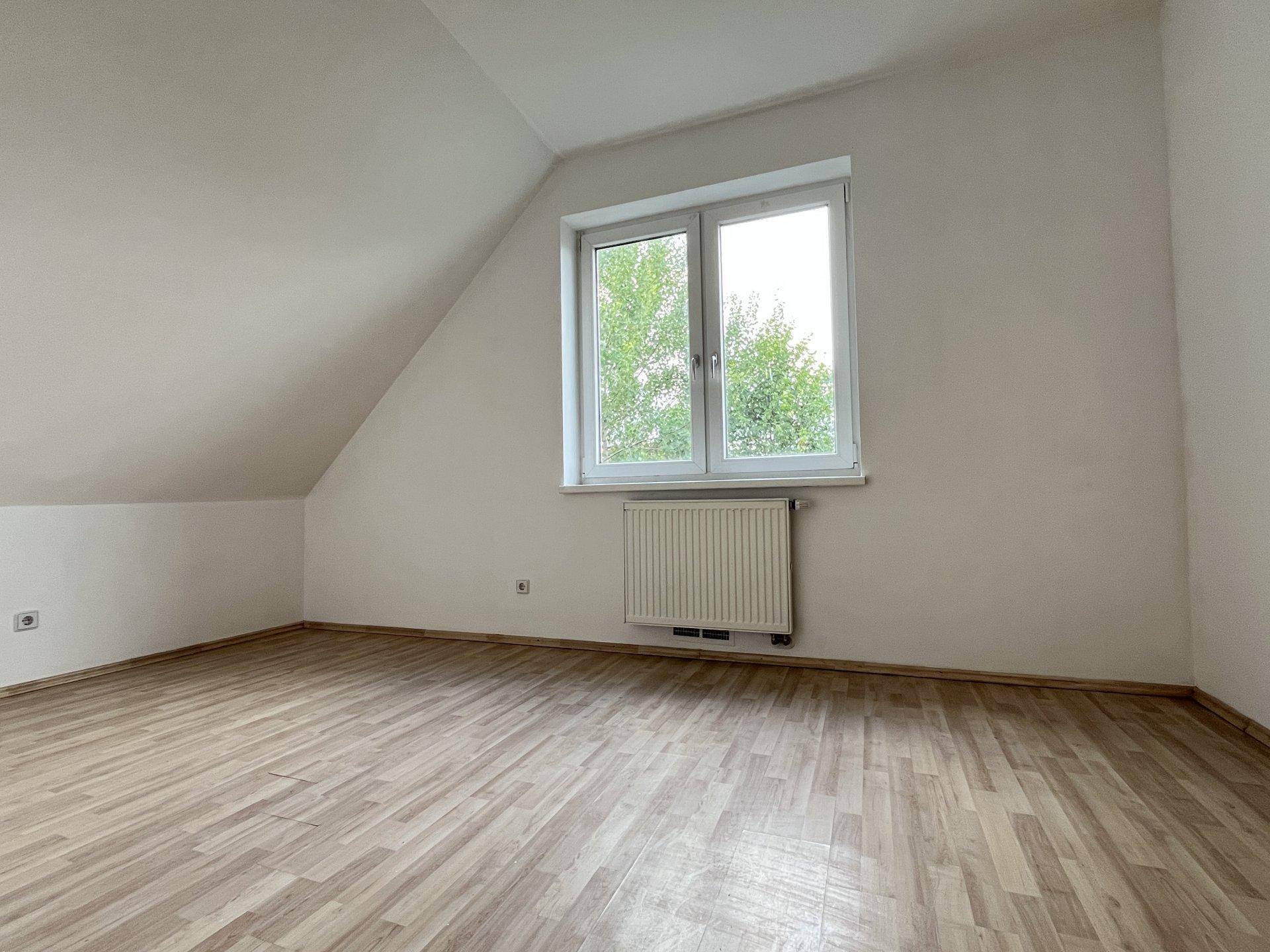 Lichtdurchflutetes Schlafzimmer mit hellem Laminatboden, Dachschräge und Blick ins Grüne.