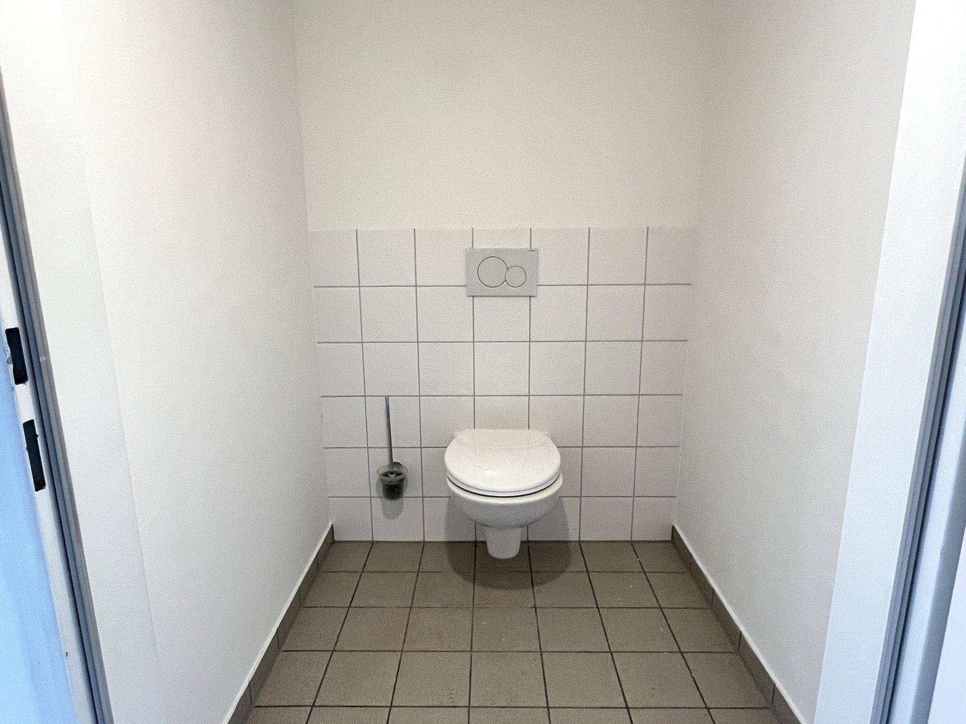 Separate Toilette mit Wand-WC und weißen Fliesen im unteren Bereich der Wände.