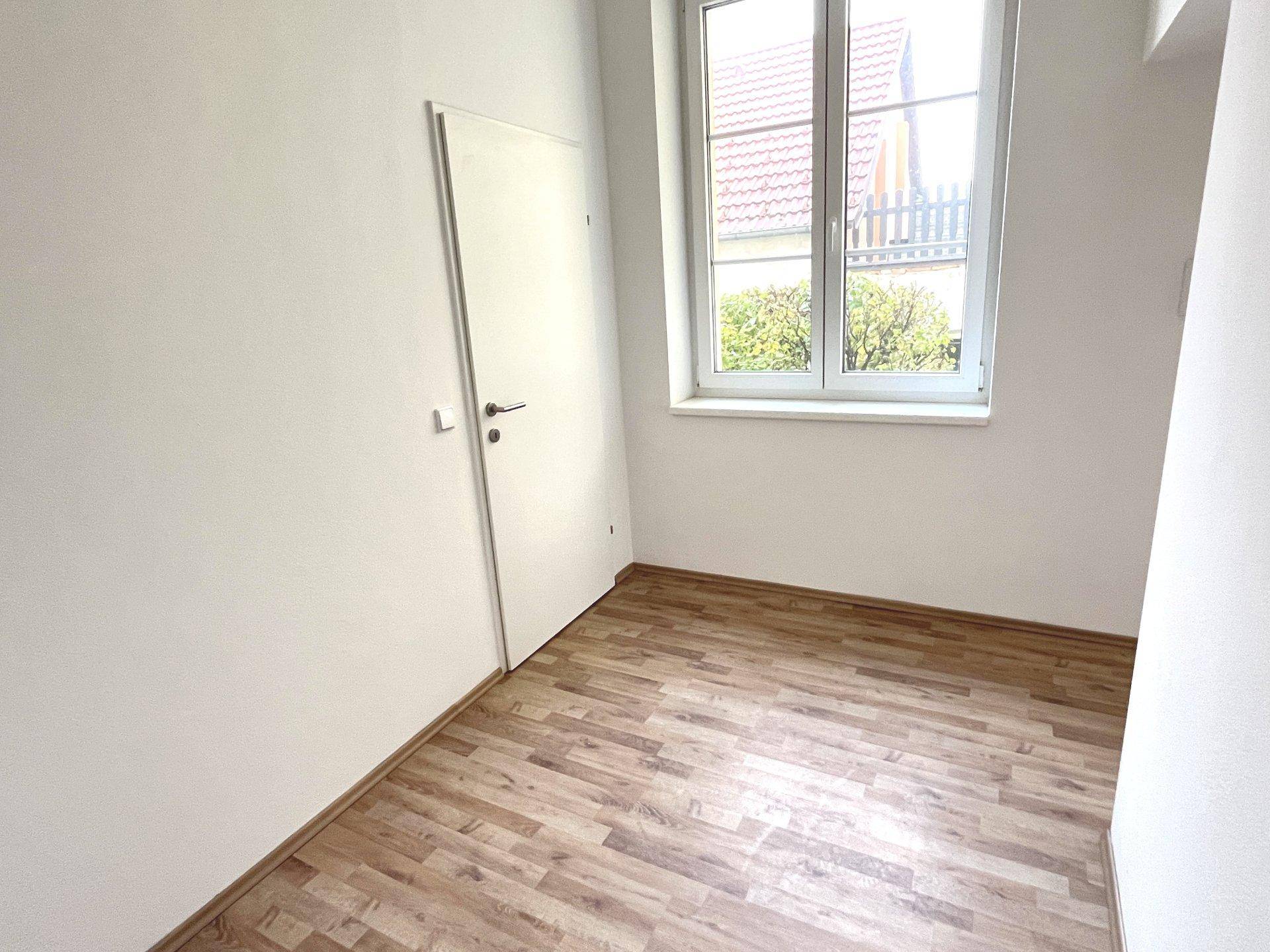 Leerer Raum mit Laminatboden, weißen Wänden und einem Fenster mit Blick auf die Umgebung.