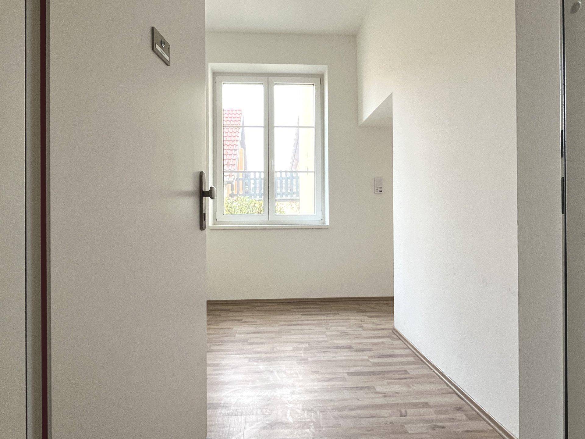 Heller Innenraum mit Laminatboden und einem Fenster, das den Blick nach draußen freigibt.