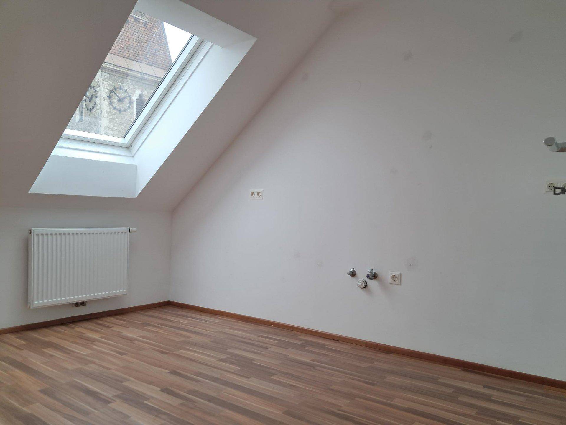 Dachgeschossraum mit einem einzelnen Dachfenster und Anschlüssen für eine mögliche Küche oder Bad.