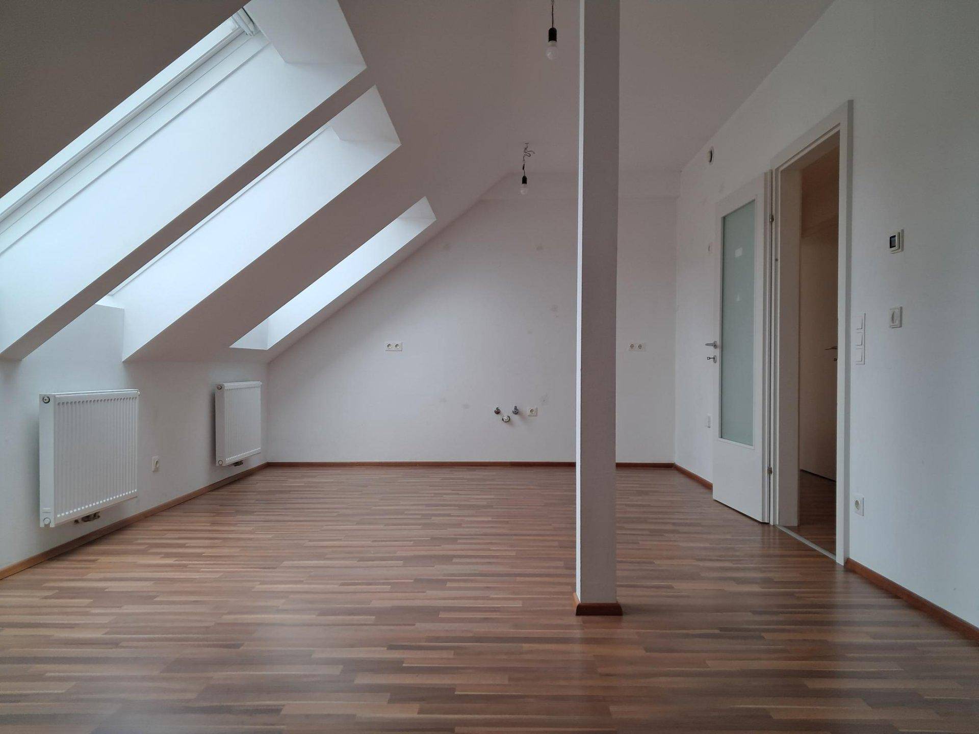 Geräumiger Dachgeschossraum mit mehreren Dachfenstern, Holzboden und einer tragenden Säule.