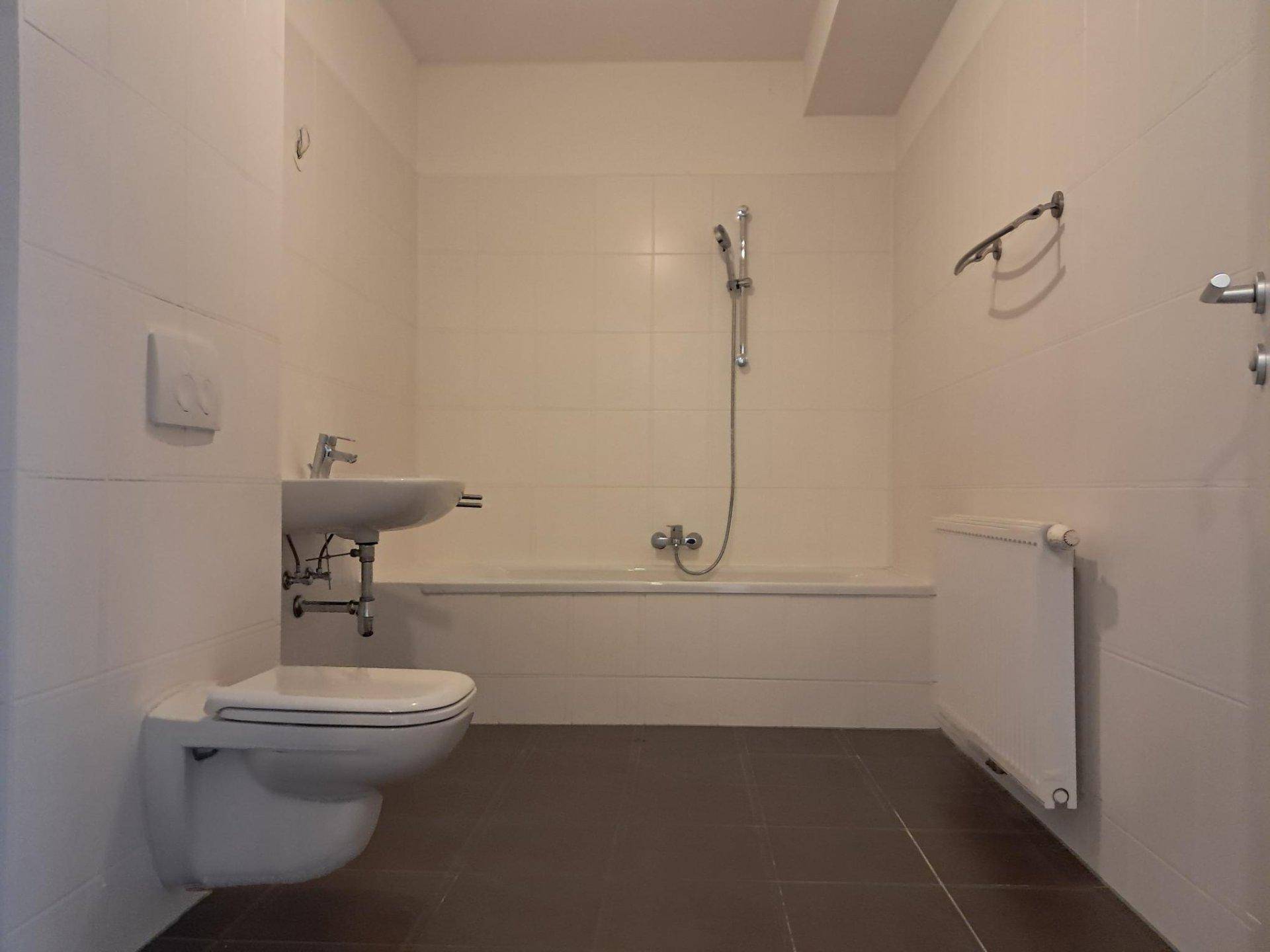 Funktionales Badezimmer mit Badewanne, Waschbecken, Toilette und dunklen Bodenfliesen.