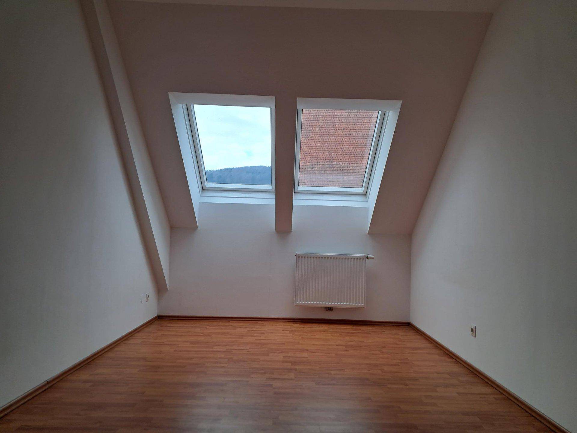 Dachgeschosszimmer mit zwei Dachfenstern, die einen Blick auf die Landschaft und den Himmel bieten.